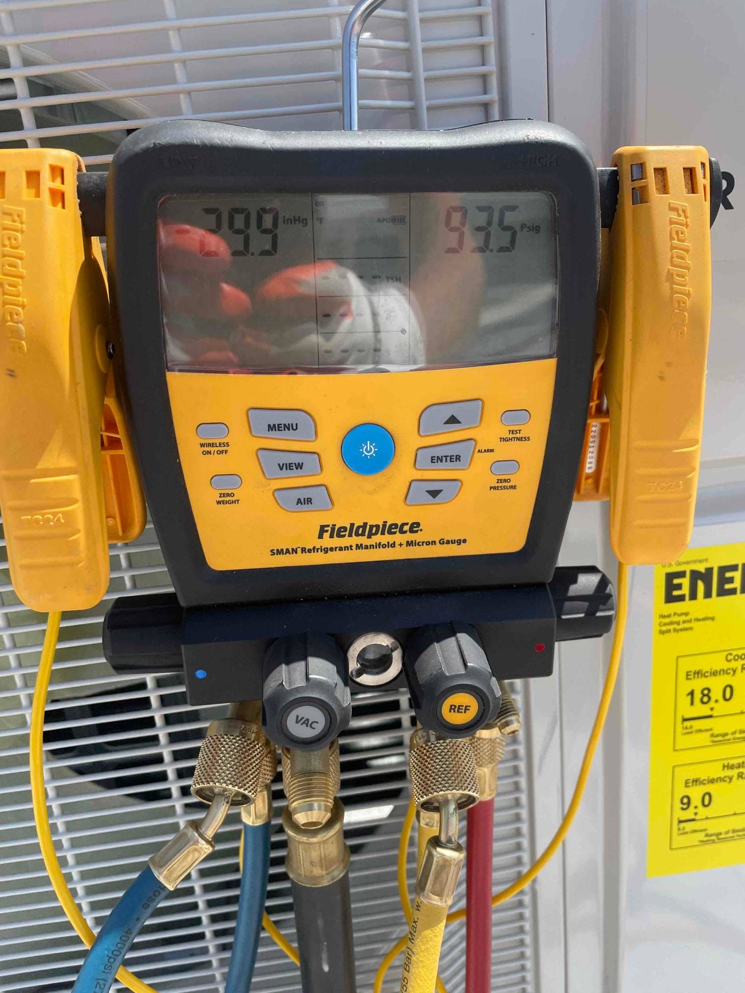 Digital manifold connected to the outdoor unit shows readings while technicians commission the system.