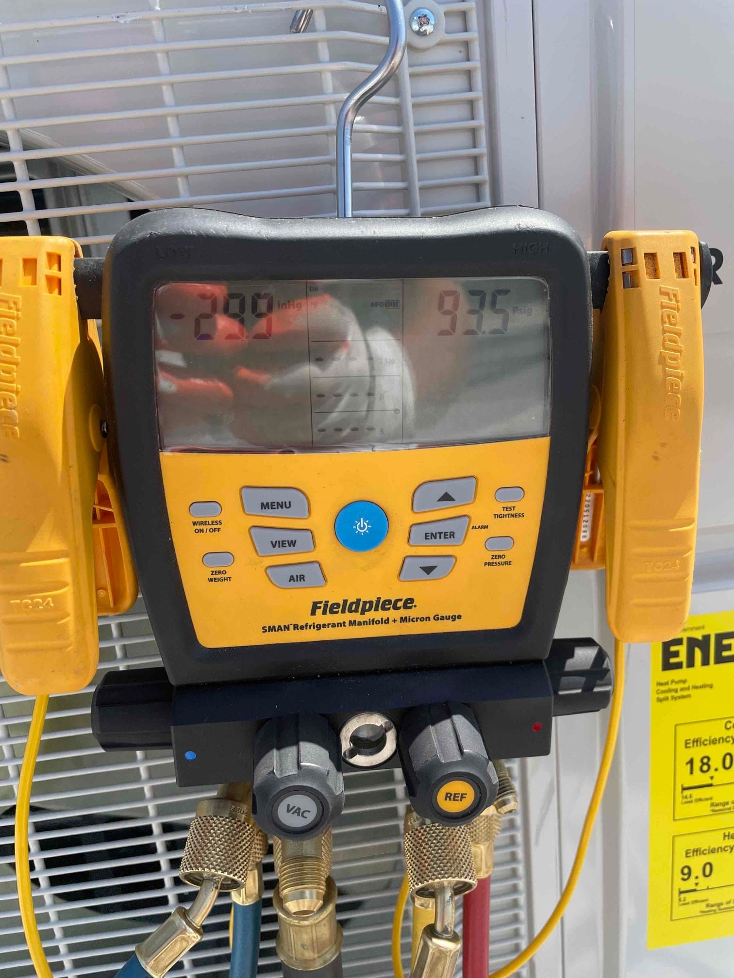Digital refrigerant manifold connected at the outdoor unit, showing screen readings and attached temperature clamps during setup.