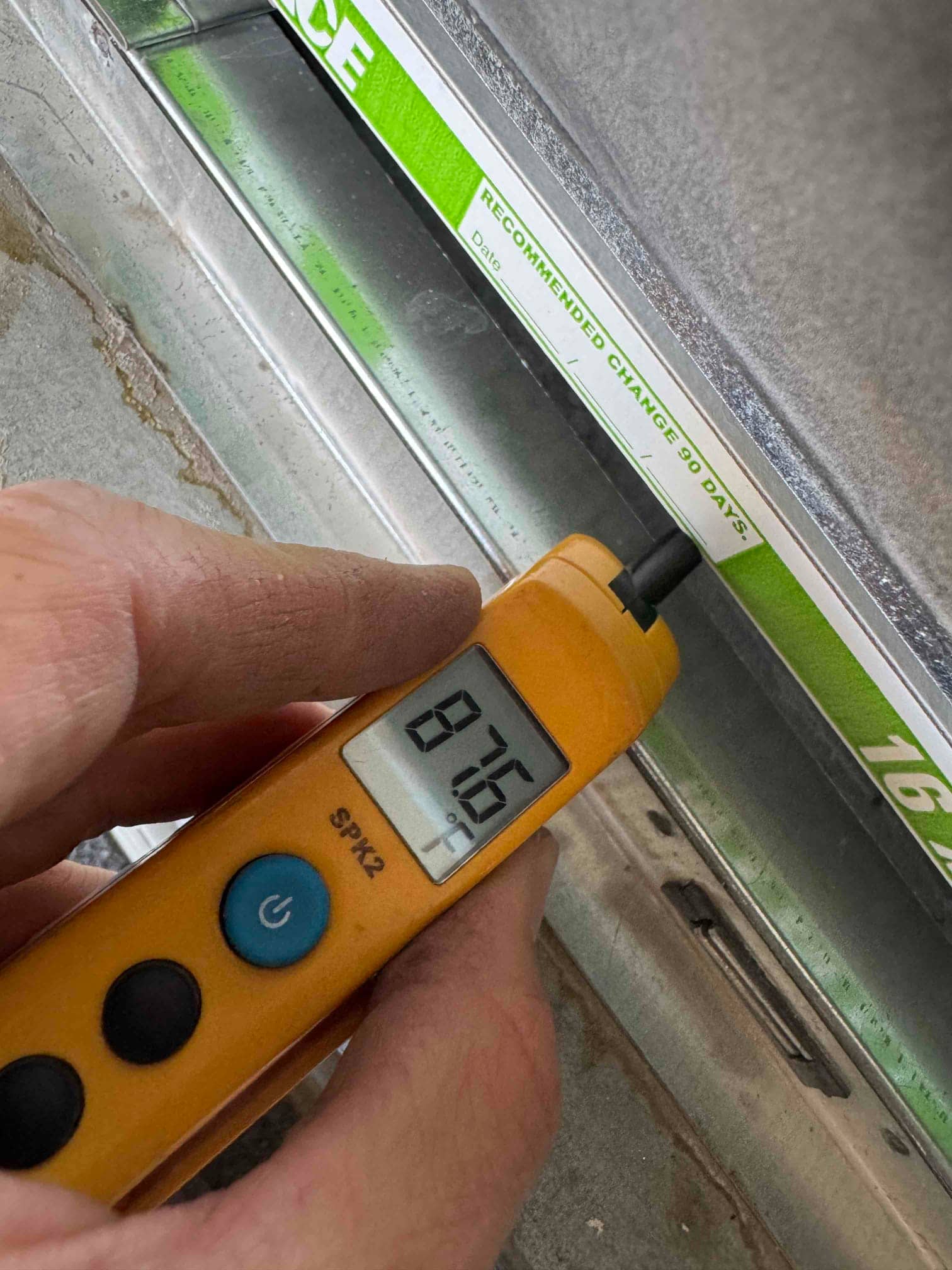 Digital thermometer shows 87.6 °F air temperature at the return filter during system operation.