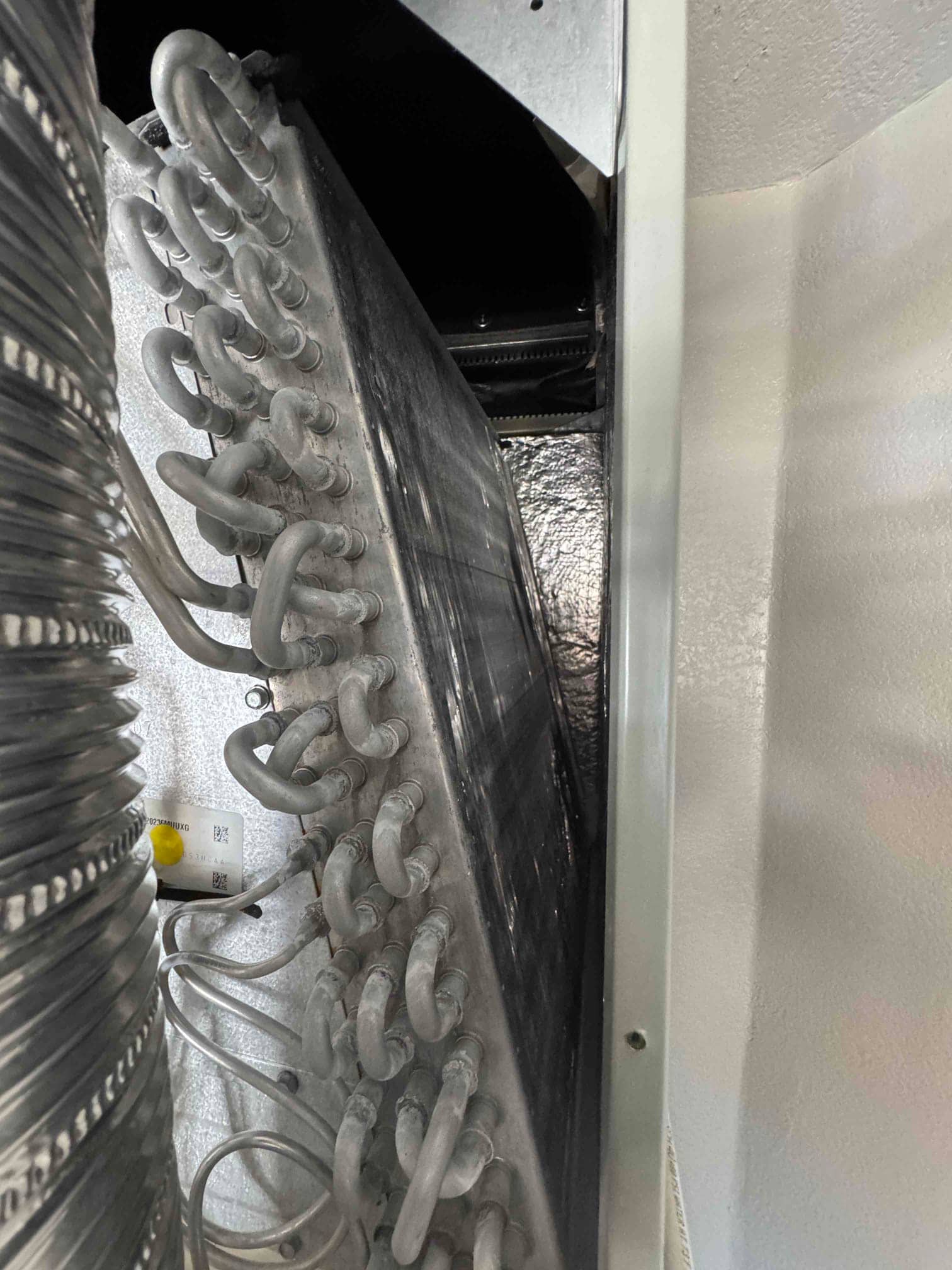Evaporator coil housing open, showing frosted coil surface and refrigerant tubing loops before thawing and cleaning.