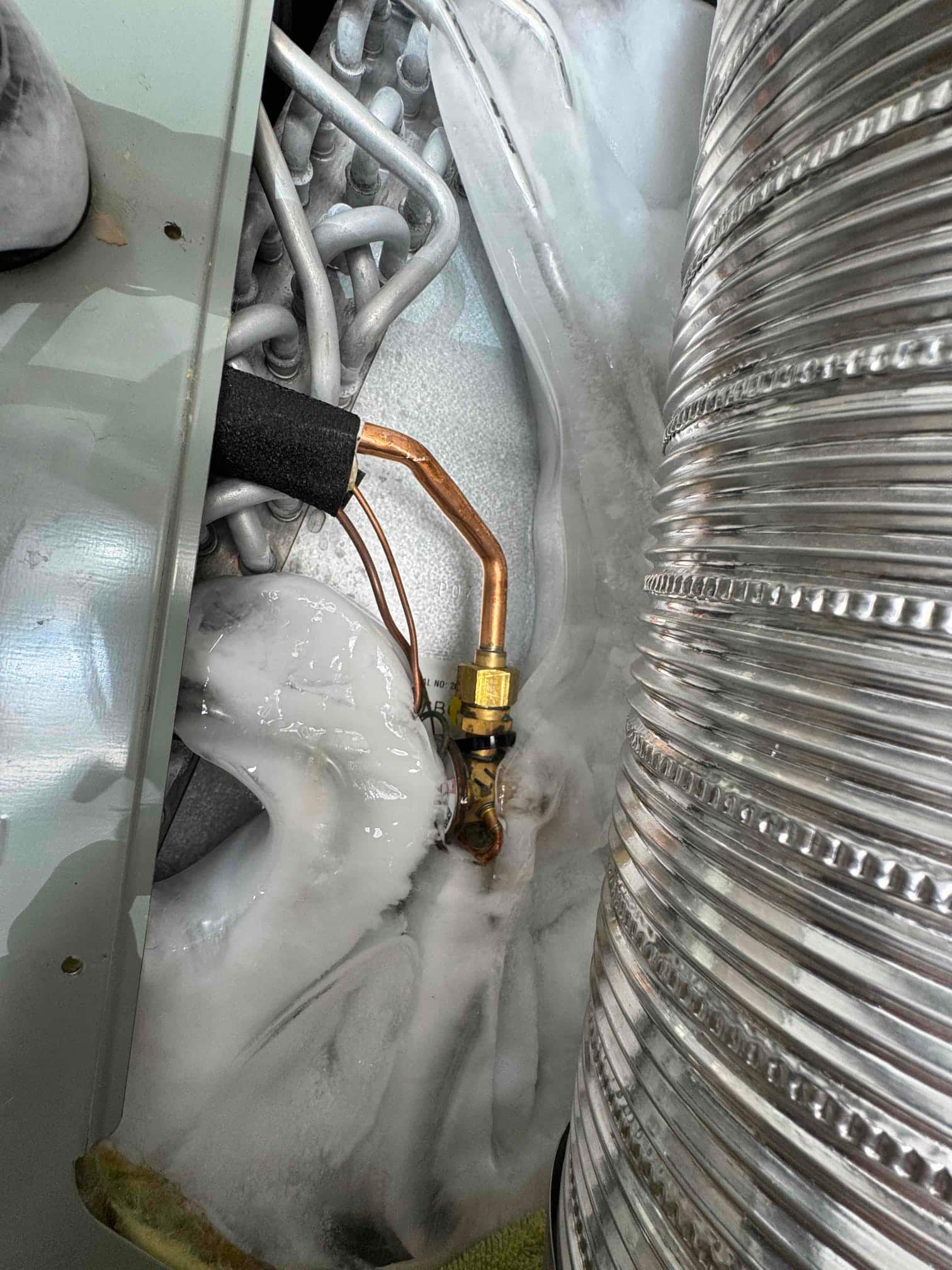 Evaporator section with heavy ice buildup on copper lines and coil surfaces, indicating frozen evaporator requiring thaw and cleaning.
