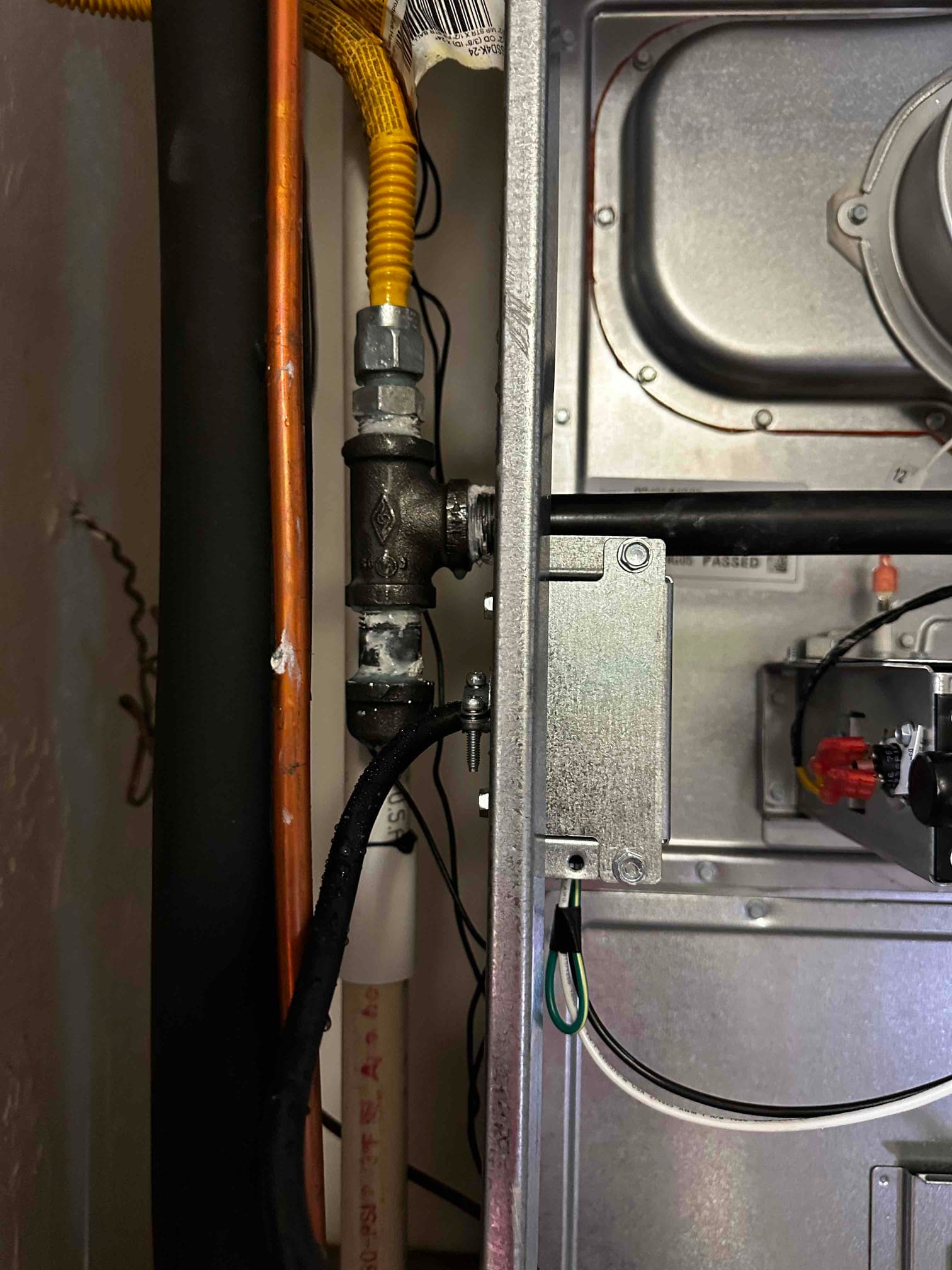 Gas furnace gas line with sediment trap and flexible connector adjacent to refrigerant and condensate drain lines inside the cabinet.