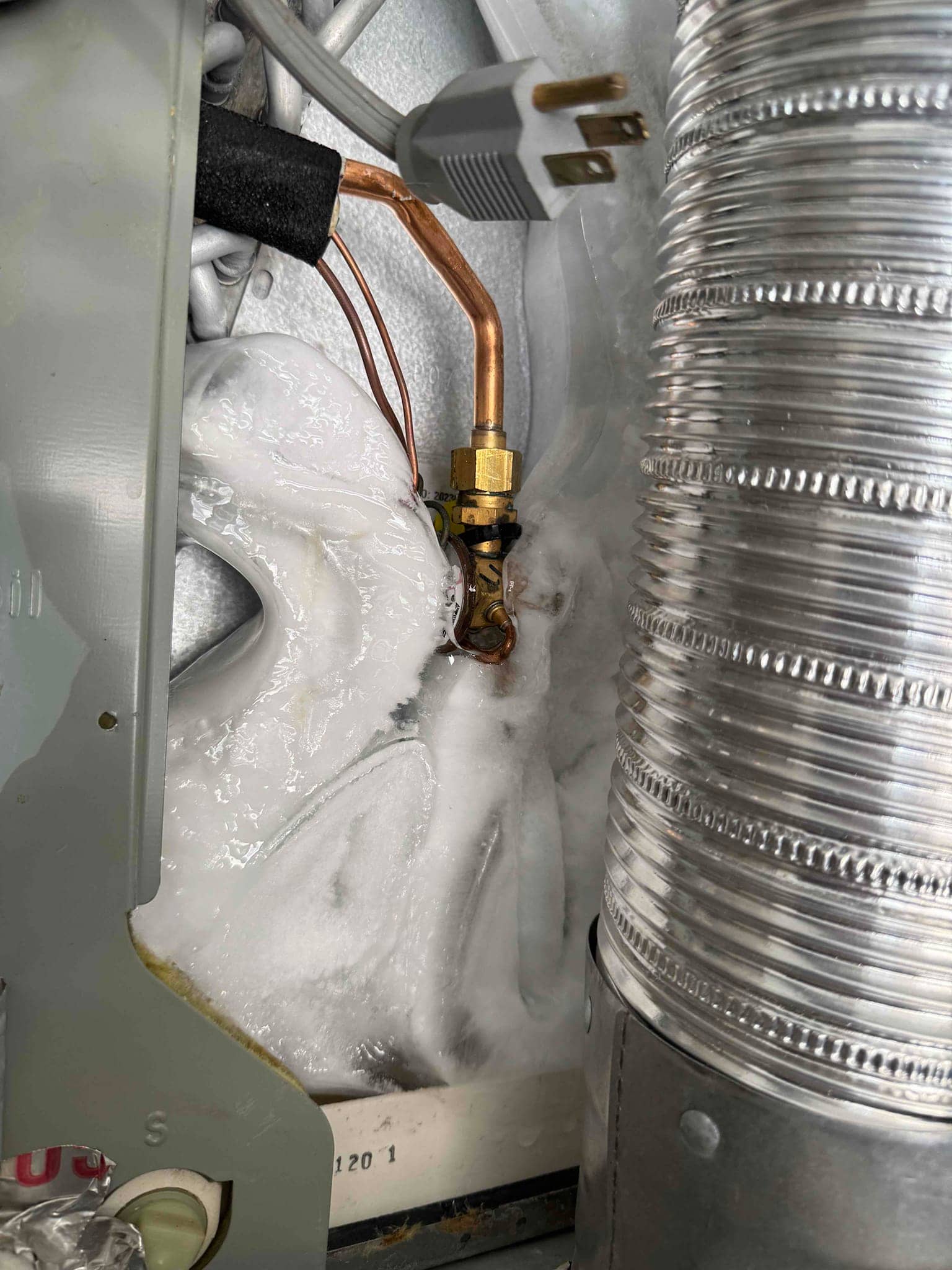Indoor evaporator section with heavy ice buildup on the copper refrigerant line and coil surface near the expansion valve.