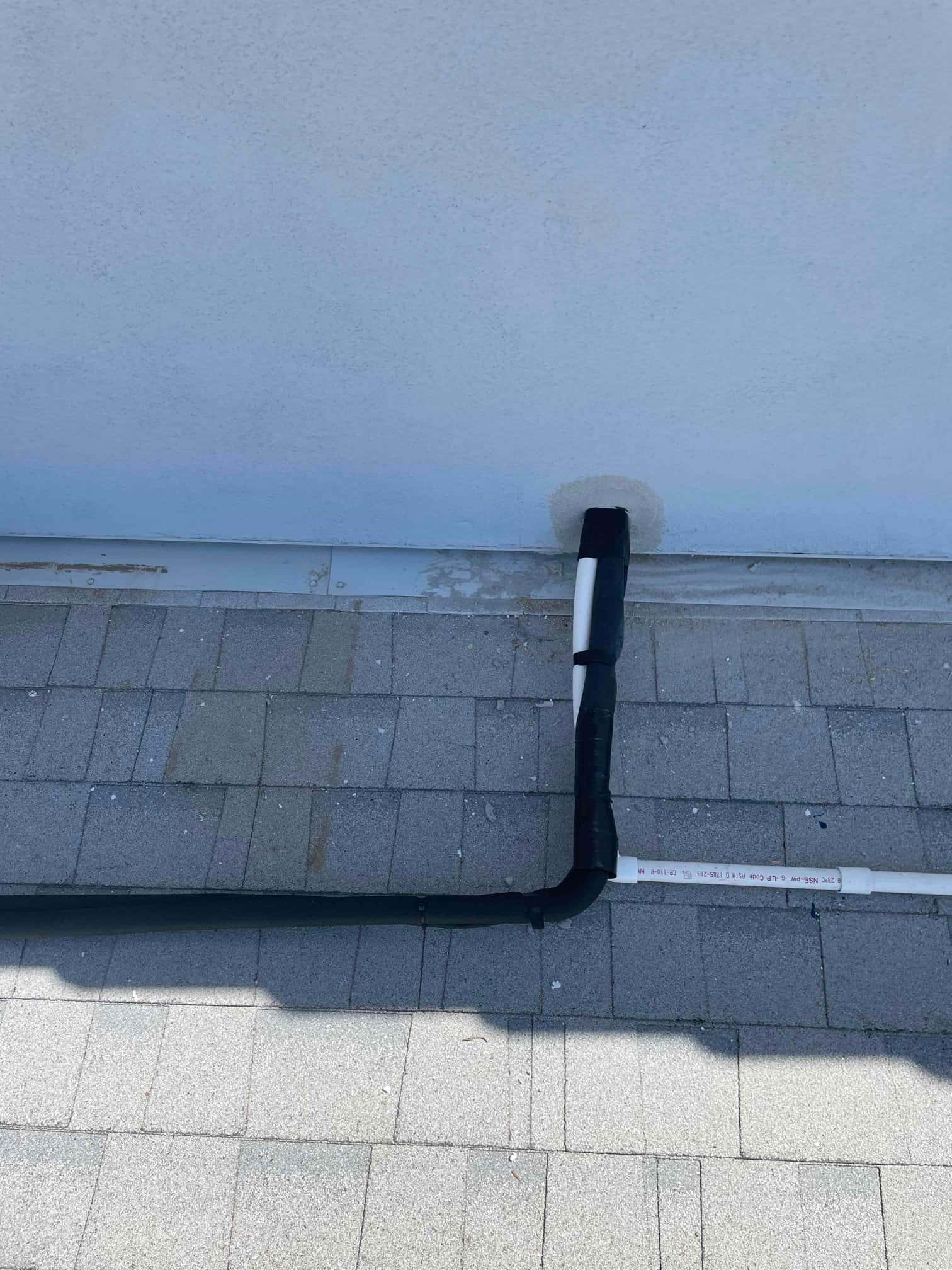 Insulated refrigerant line set and PVC condensate drain routed across roof and sealed at wall penetration.