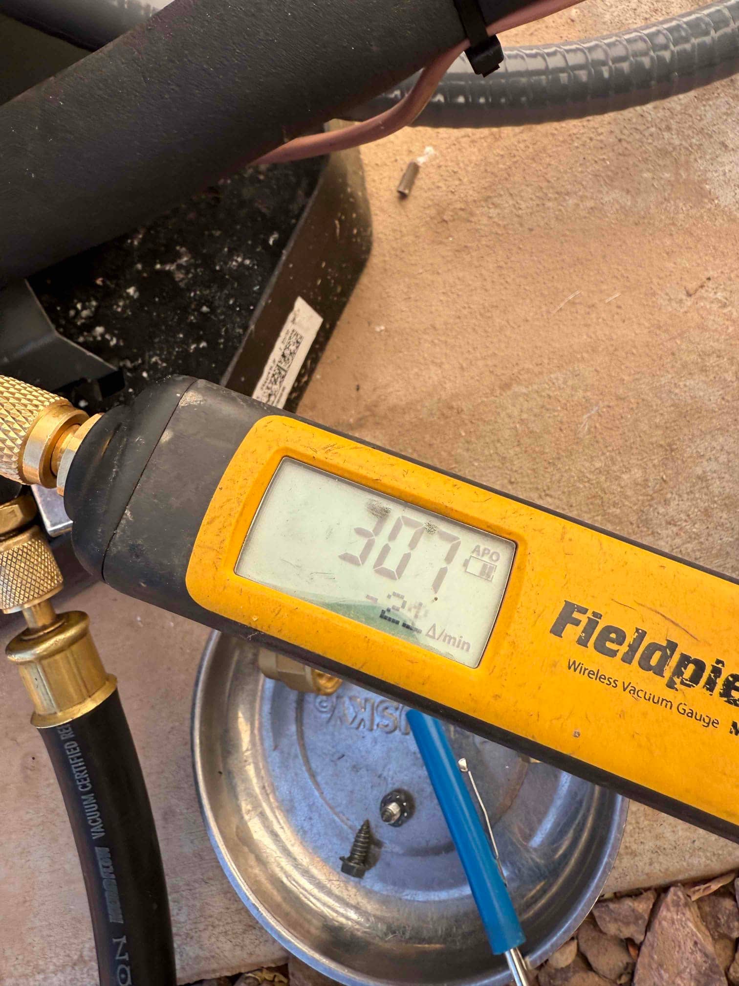 Micron gauge connected during evacuation shows 307 microns, documenting a deep vacuum before opening the refrigerant charge.