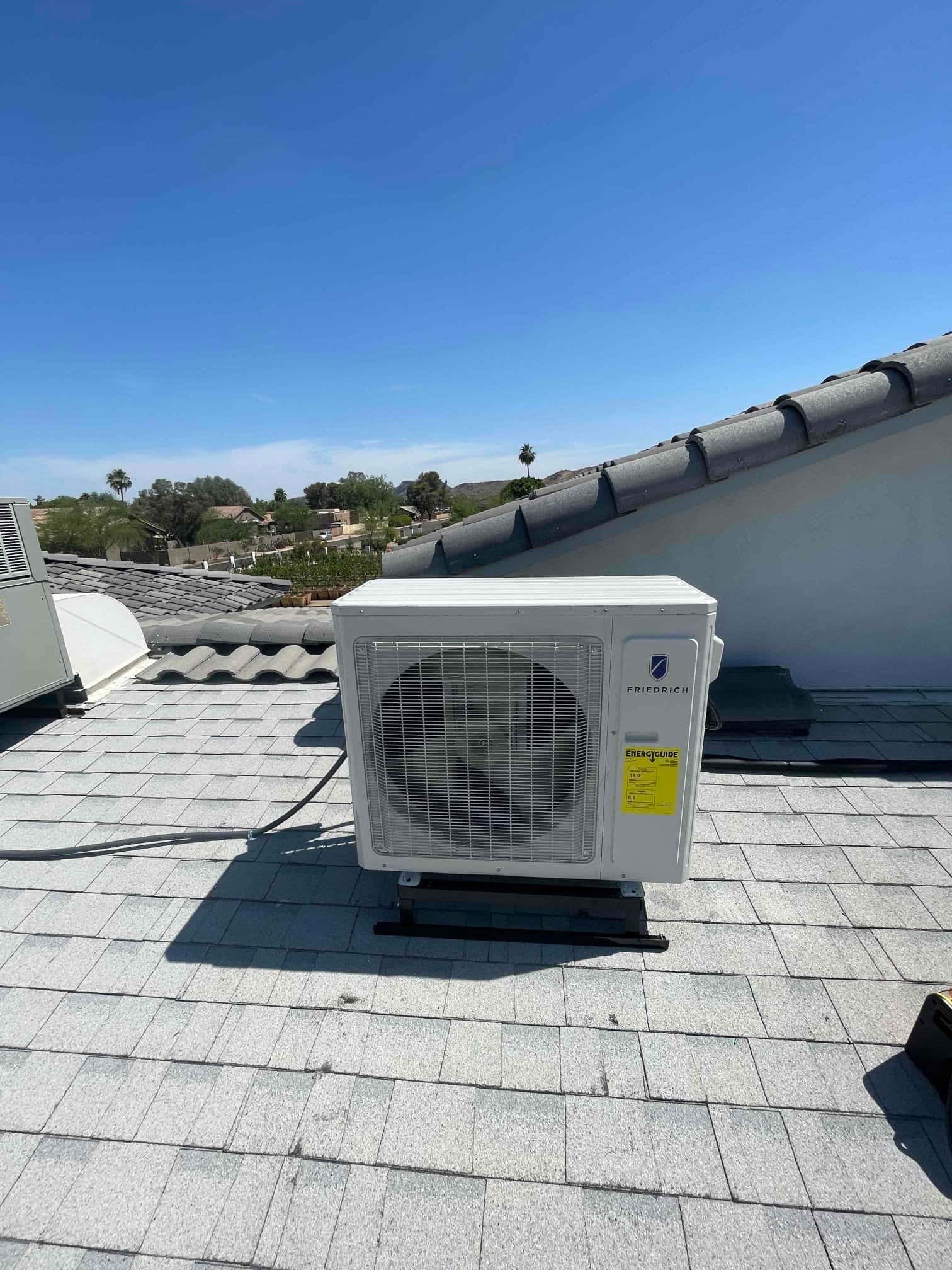 Mini-split outdoor condenser set on roof-mounted supports with insulated line set routed along the shingles.