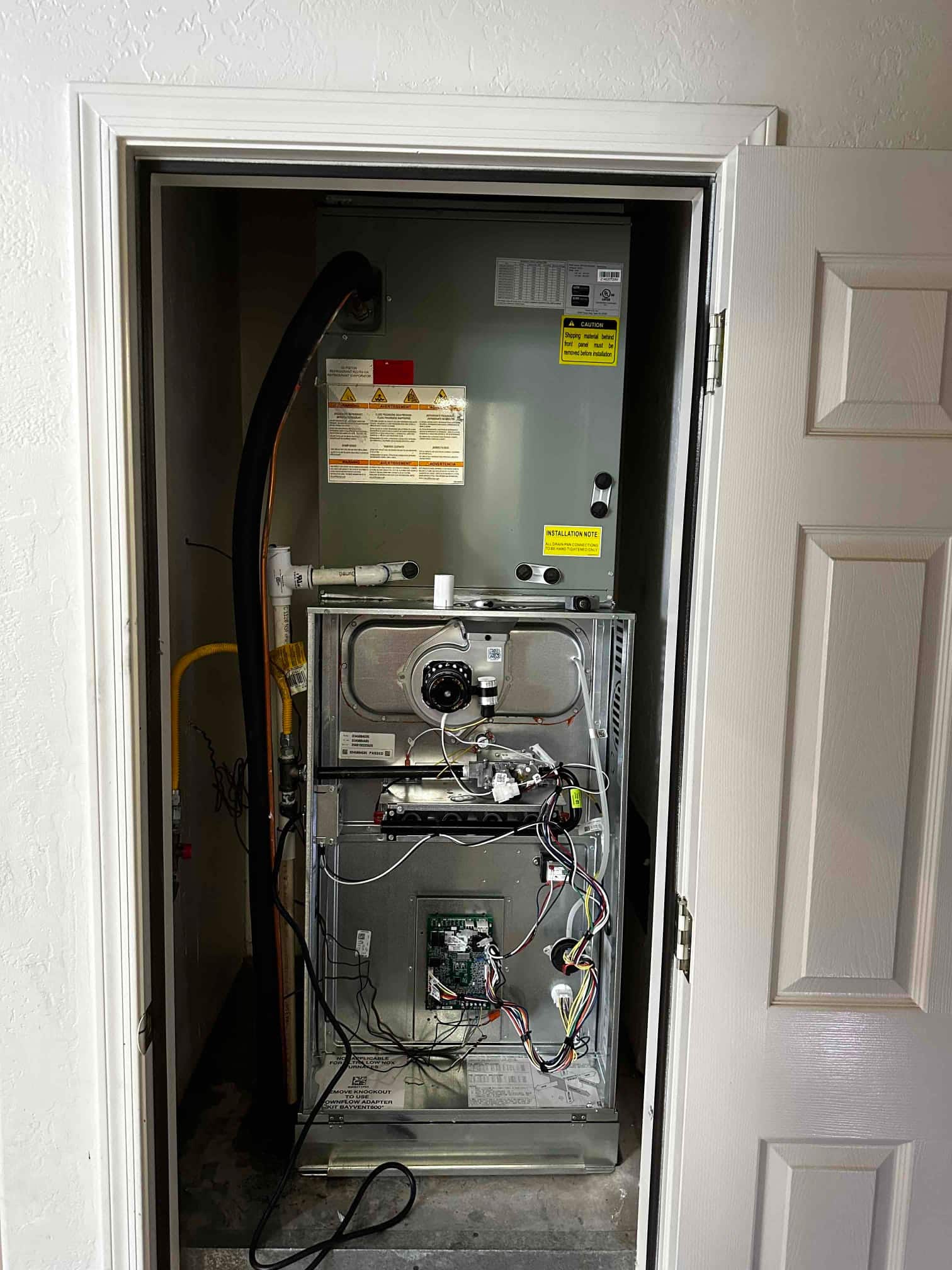 New furnace and evaporator installed in a closet, with wiring accessible and condensate drain piping connected for commissioning.