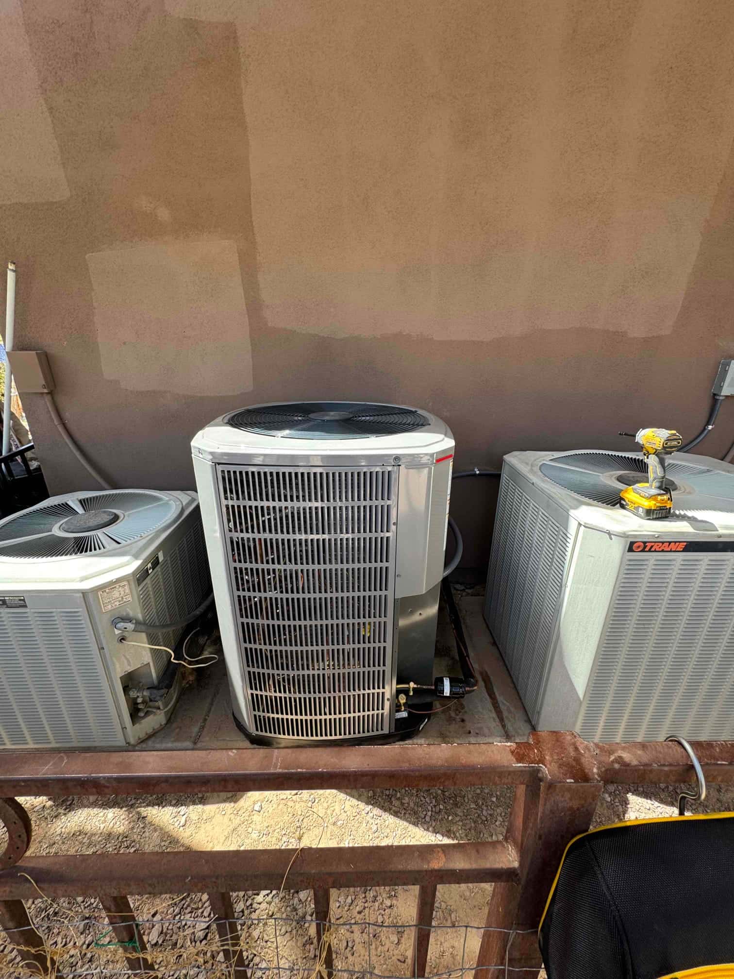 New outdoor heat pump condenser set on a level pad between two existing units, with insulated line set and disconnect nearby.