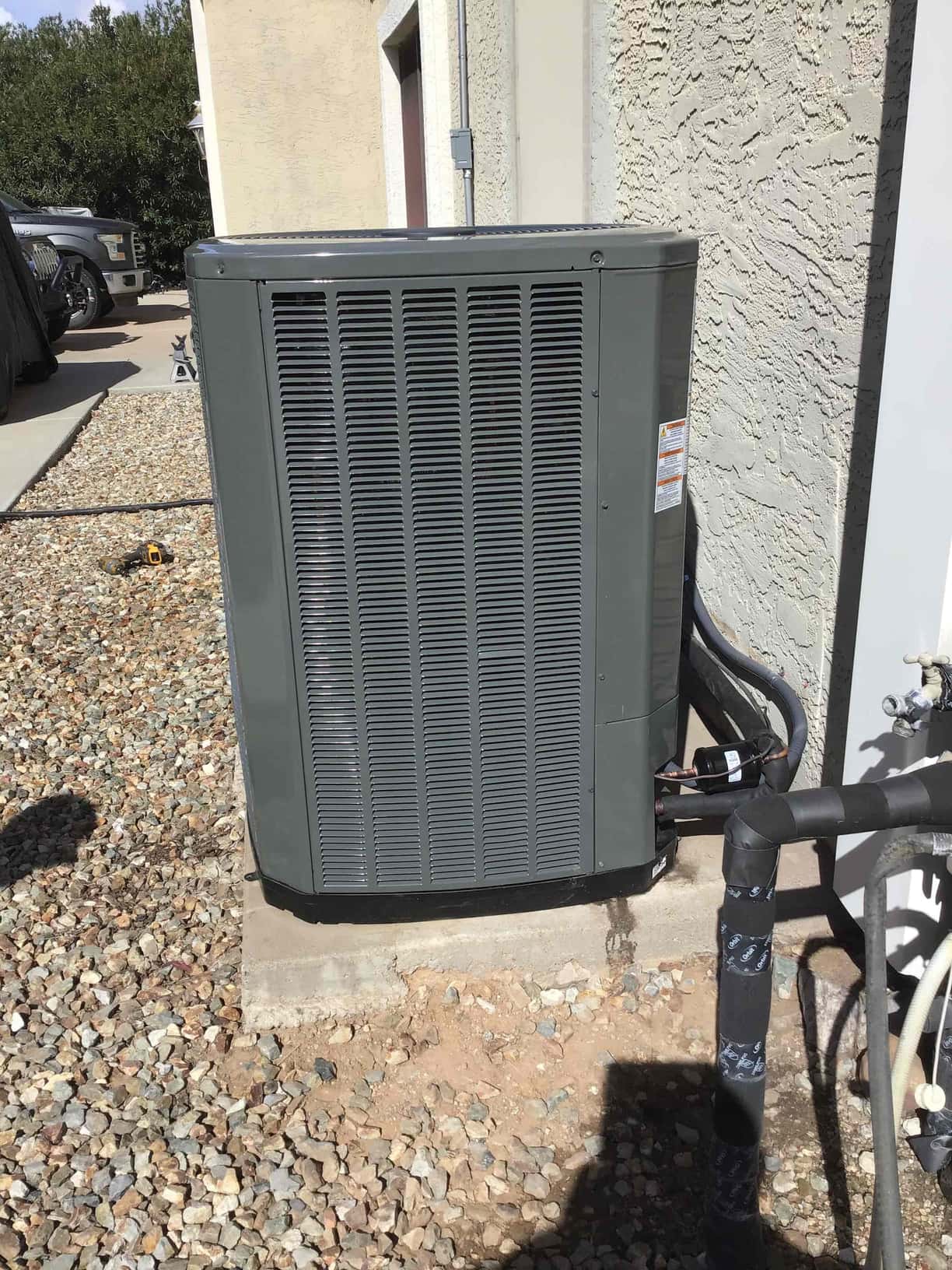 New outdoor heat pump condenser set on a level pad with insulated refrigerant lines and sealed wall penetration.