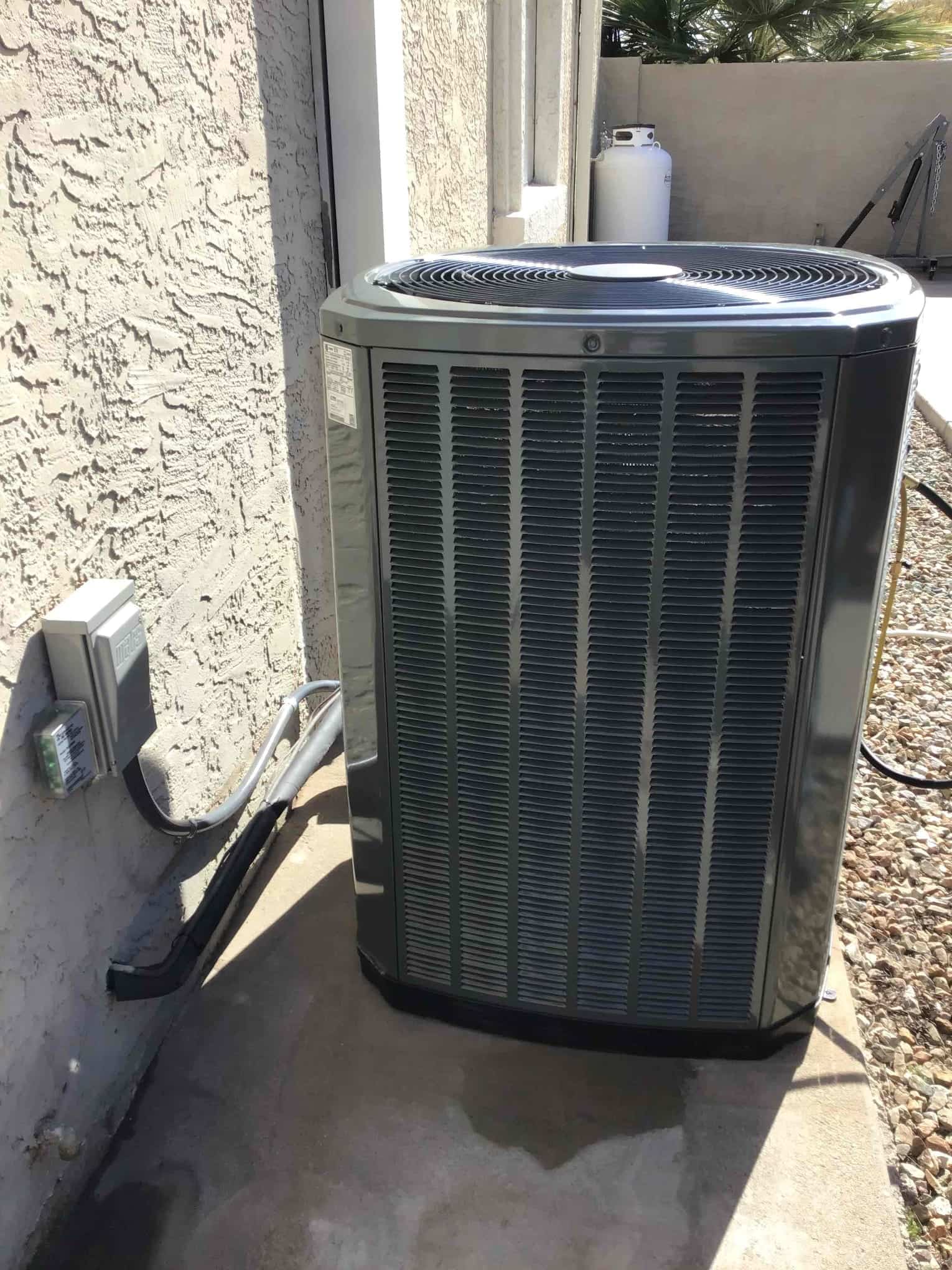 New outdoor heat pump condenser set on a level pad with insulated line set and exterior disconnect box installed.