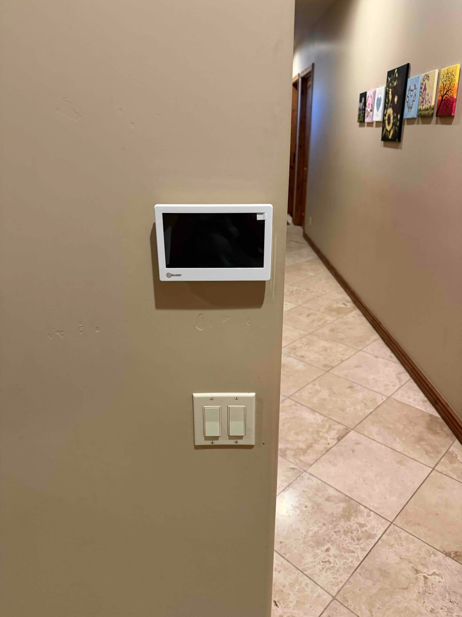 New wall-mounted thermostat installed cleanly in a hallway, with adjacent light switches and finished trim visible.
