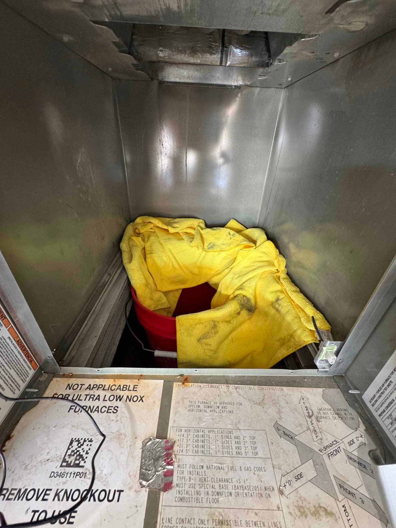 Open air handler cabinet interior with access panel removed, showing a red bucket and yellow towel catching condensate and debris.