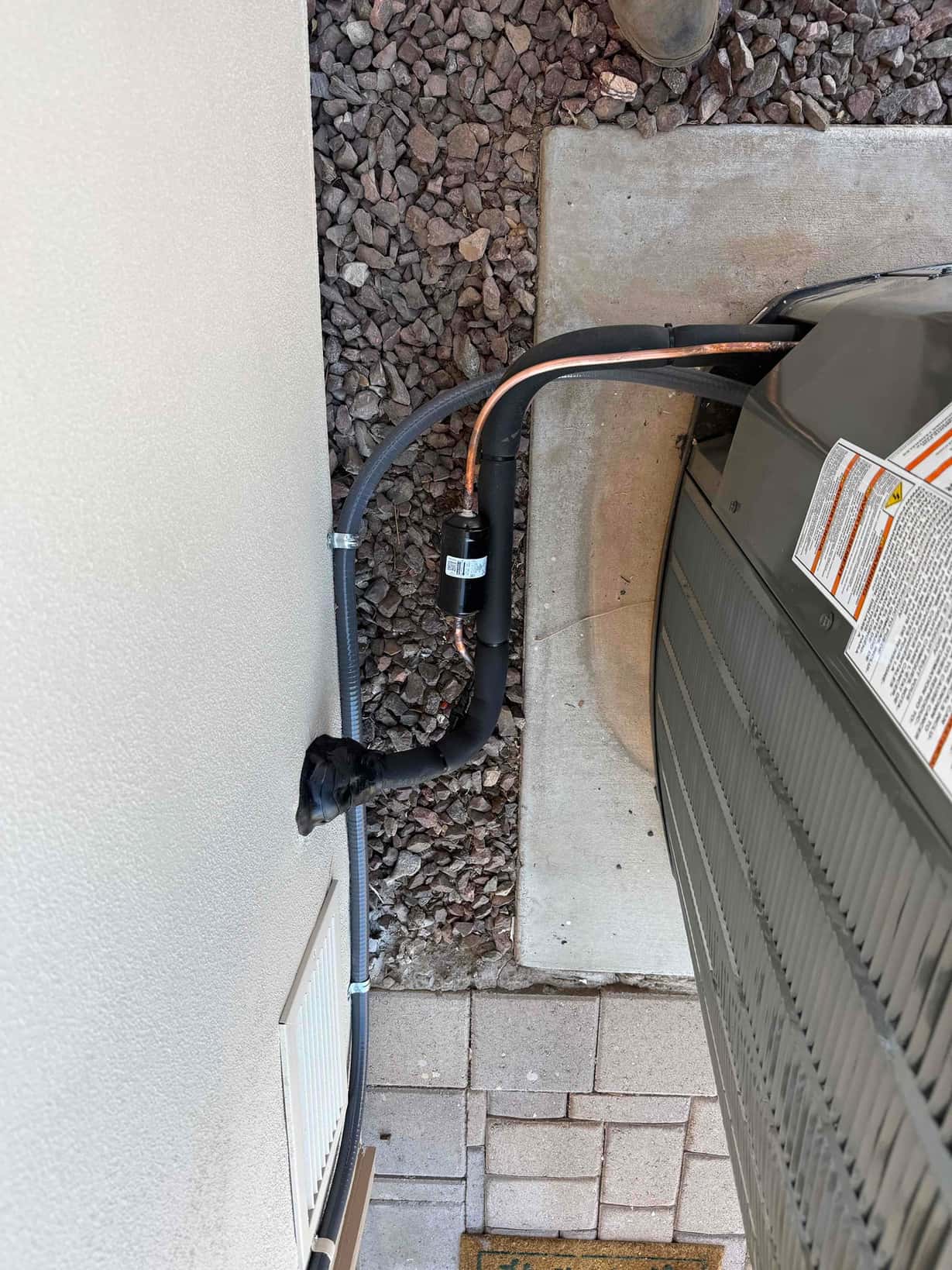 Outdoor condenser set on a level pad with insulated refrigerant line set, filter drier, and sealed wall penetration.