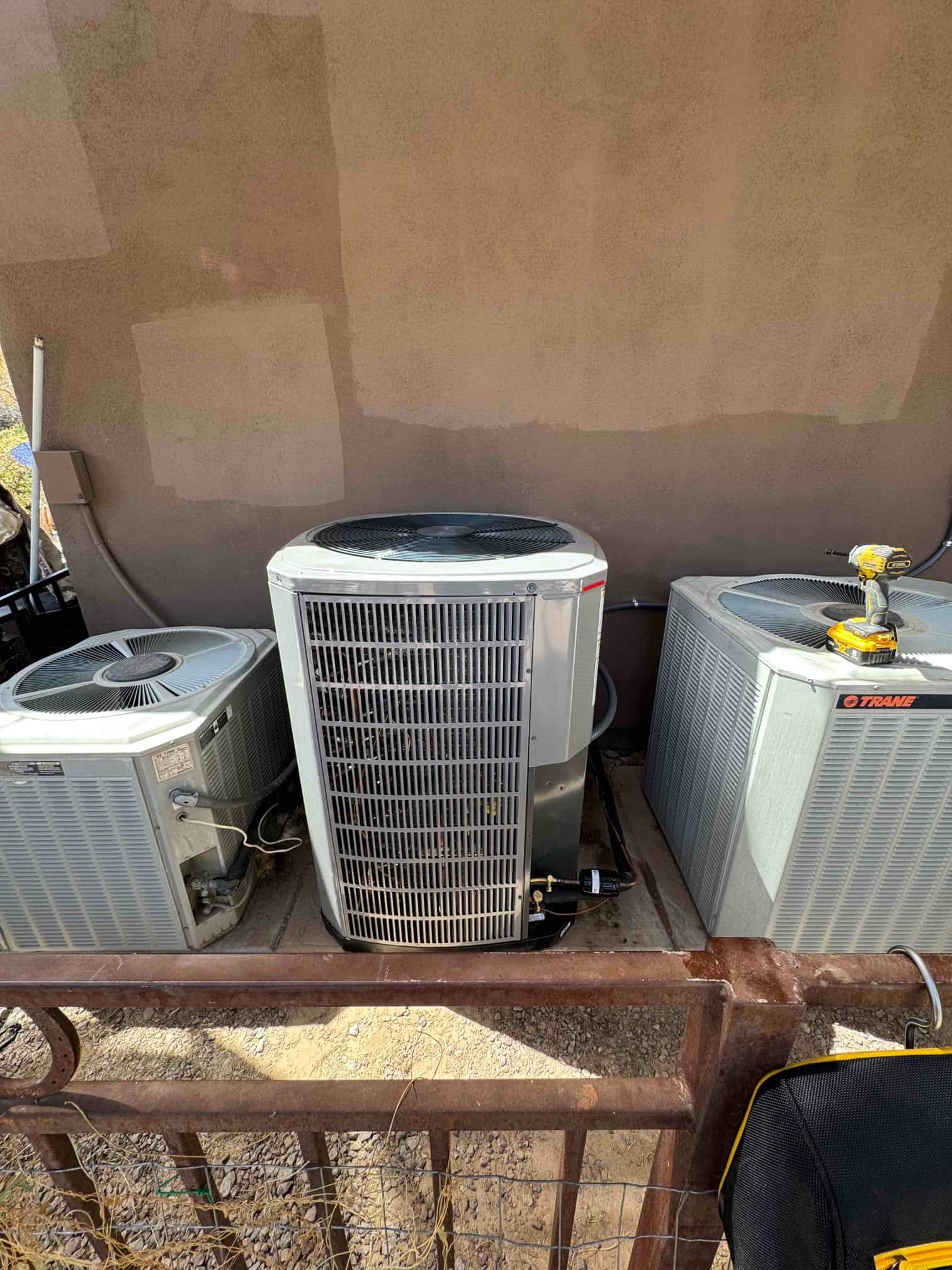 Outdoor condensers set on a pad behind a protective fence, with refrigerant lines and electrical whip connections visible.