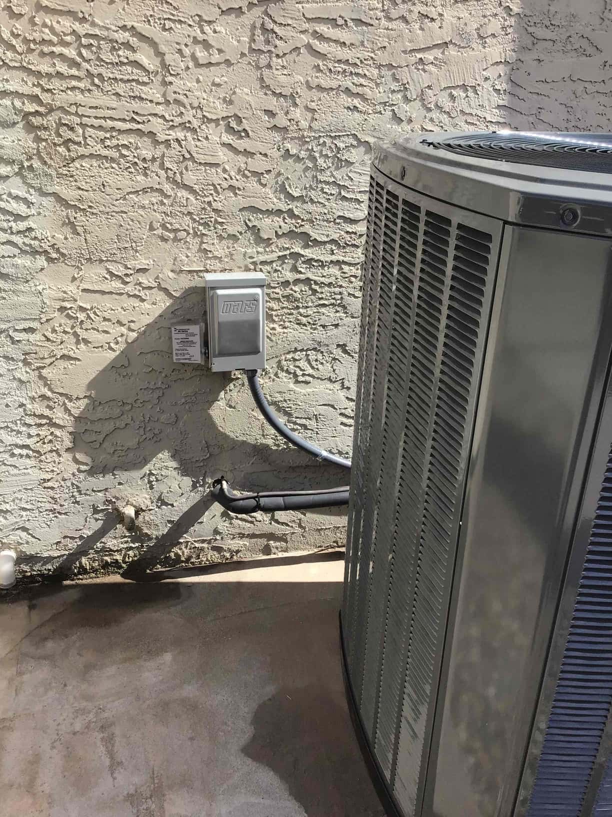 Outdoor heat pump condenser set beside the house with new weatherproof disconnect, whip, and insulated line set routed to the wall.