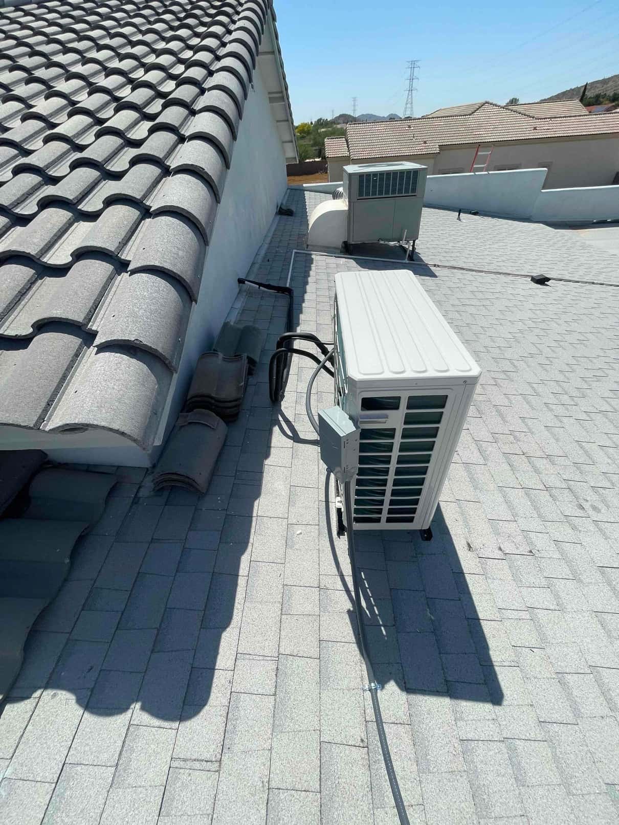 Rooftop mini-split condenser installed on shingle roof with mounted disconnect and routed line set and electrical whip.