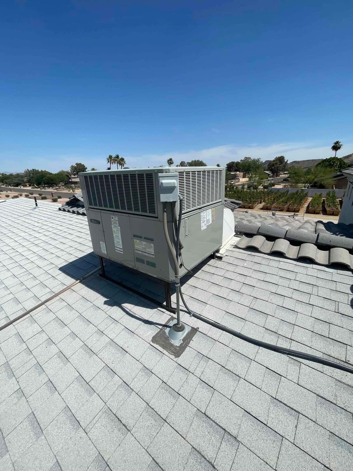 Rooftop packaged HVAC unit installed on a metal stand with electrical disconnect and sealed conduit penetration on shingle roof.
