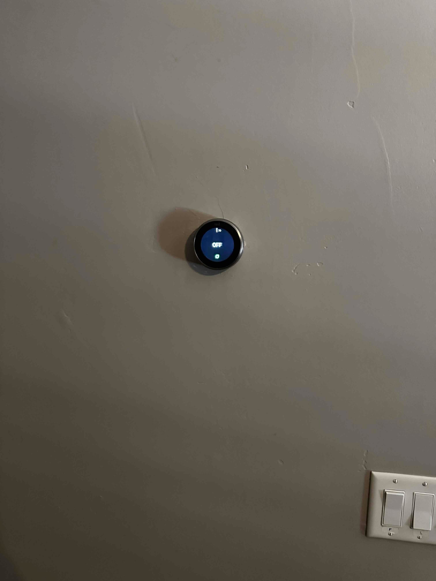 Wall-mounted smart thermostat installed and powered on, with the display indicating the system is off.