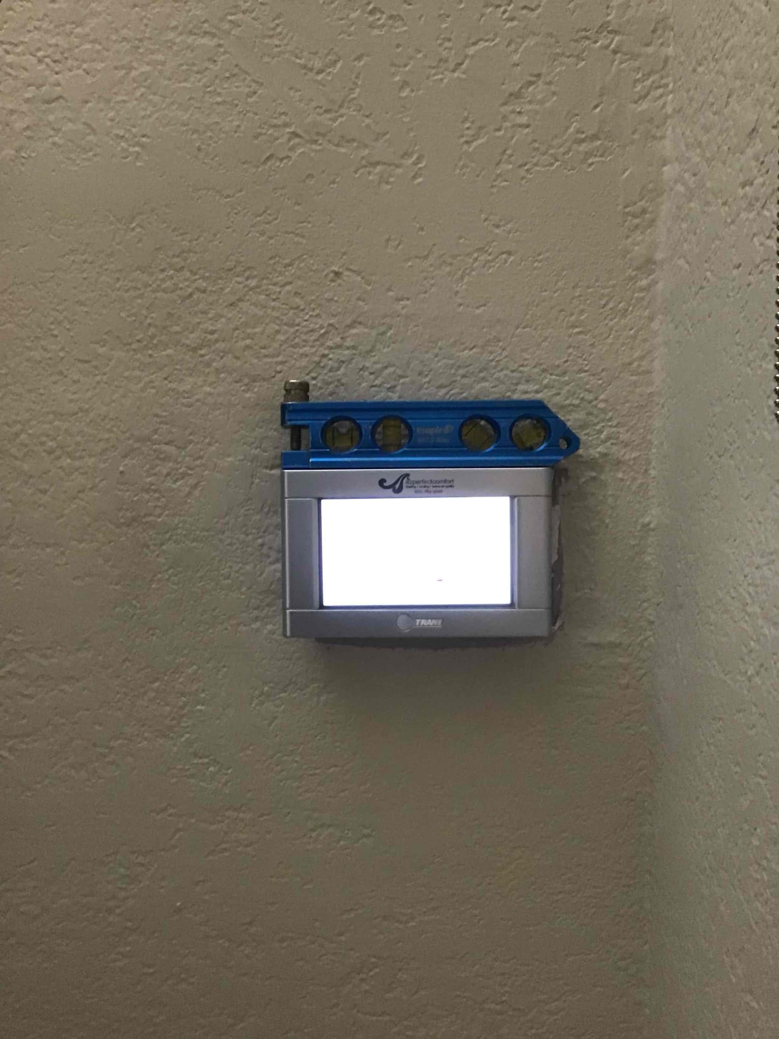 Wall-mounted thermostat installed and leveled with a bubble level positioned on top for alignment verification.