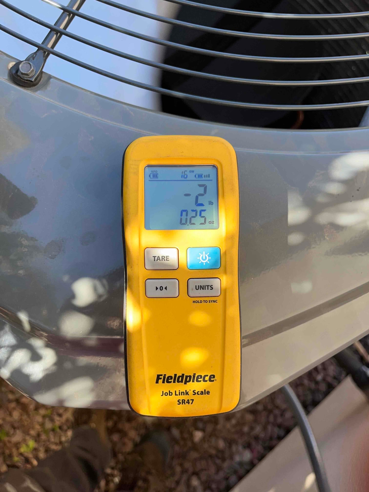 Wireless refrigerant scale display on top of the outdoor condenser shows a charge change of -2 lb 0.25 oz.
