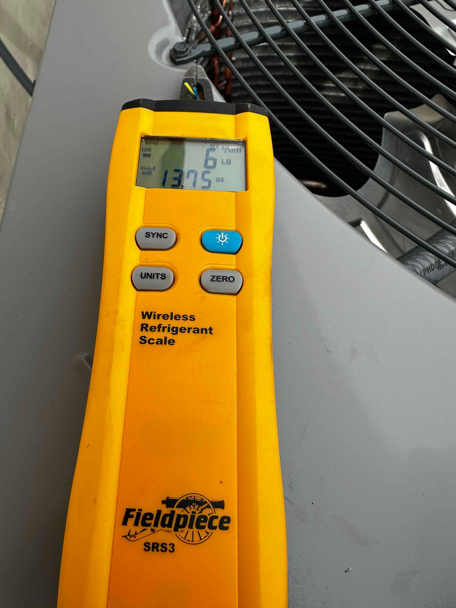 Wireless refrigerant scale on top of the outdoor unit shows a charge amount of 6 lb 13.75 oz.