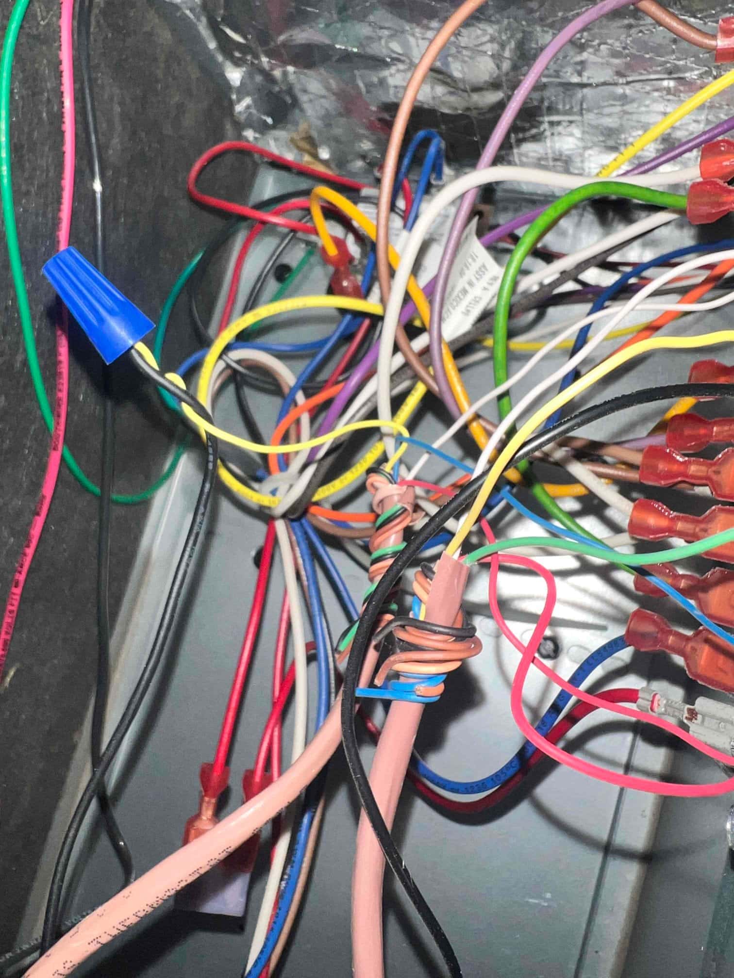 Bundle of thermostat and control wires inside an air handler junction area, with multiple wire nuts and splices visible.