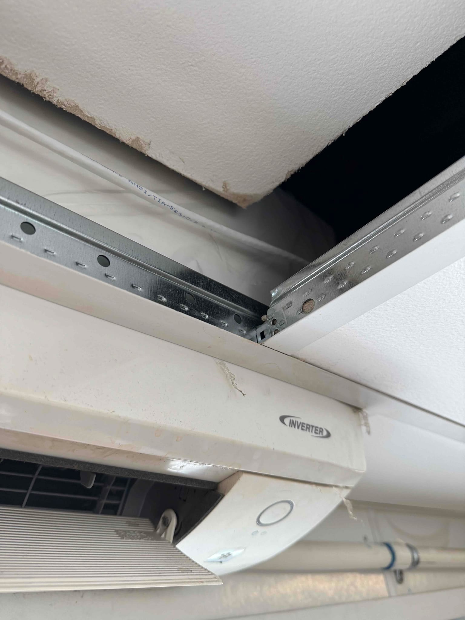 Ceiling cassette air conditioner with open access panel exposing mounting rail and ductwork above the unit.
