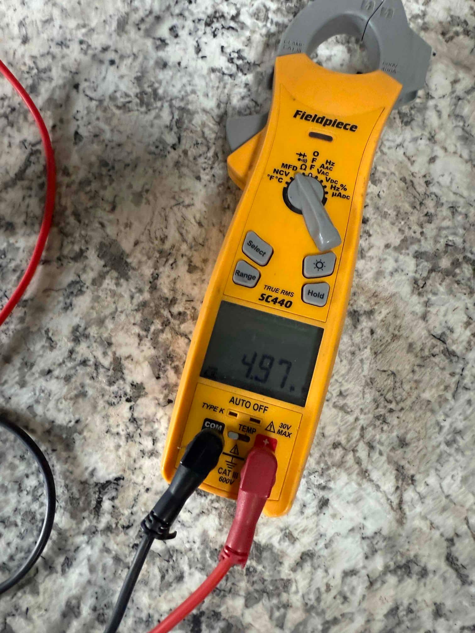 Clamp meter displays 49.7 V across the test leads while measuring voltage during the air conditioning repair.