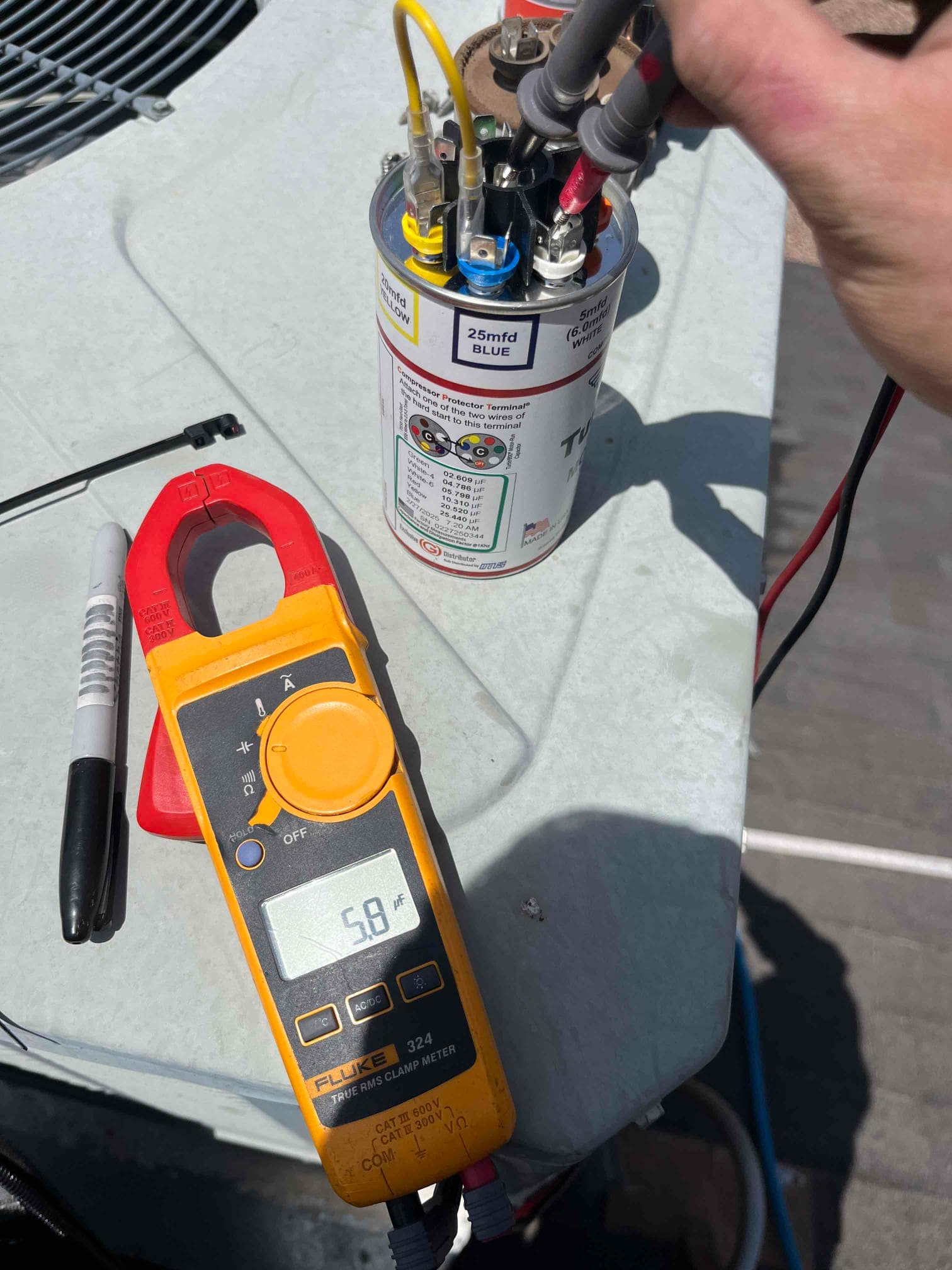 Clamp meter displays 5.8 A on a conductor while testing near a dual-run capacitor with connected leads.