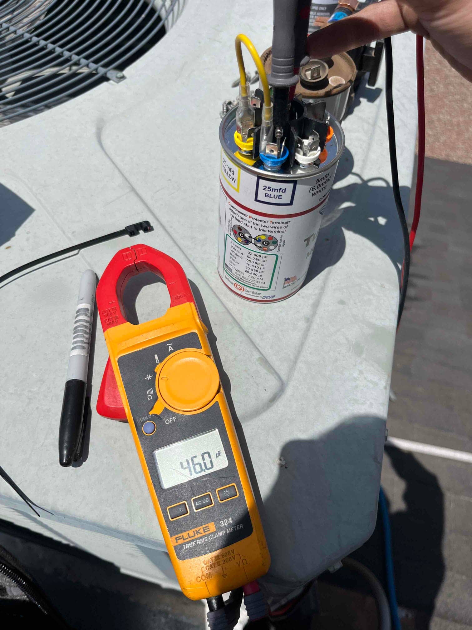 Clamp meter measures the dual-run capacitor at 46.0 µF while leads are connected to its terminals on the condenser.