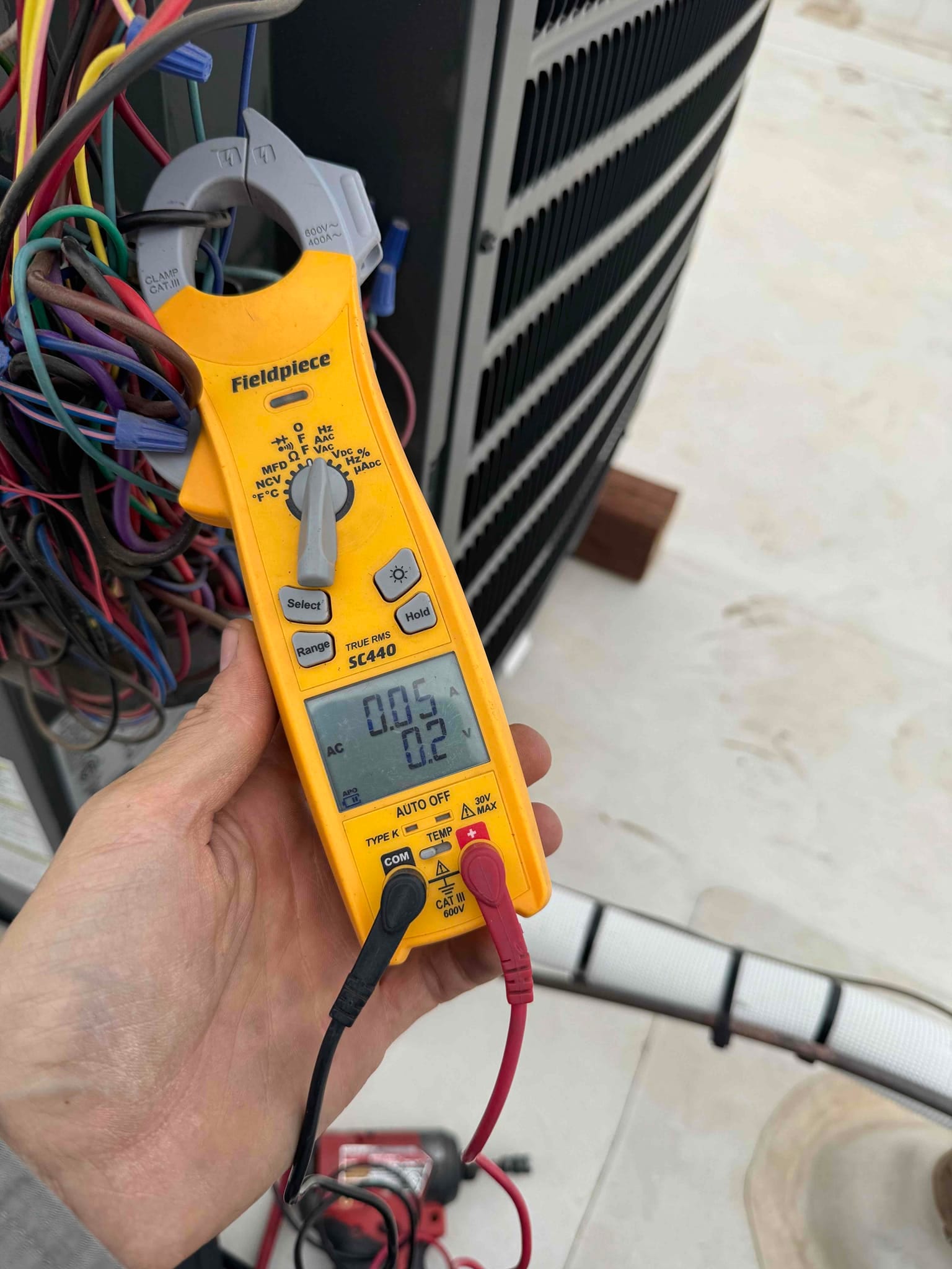 Clamp meter shows 0.5 A on a lead at the outdoor condenser unit during measurement.