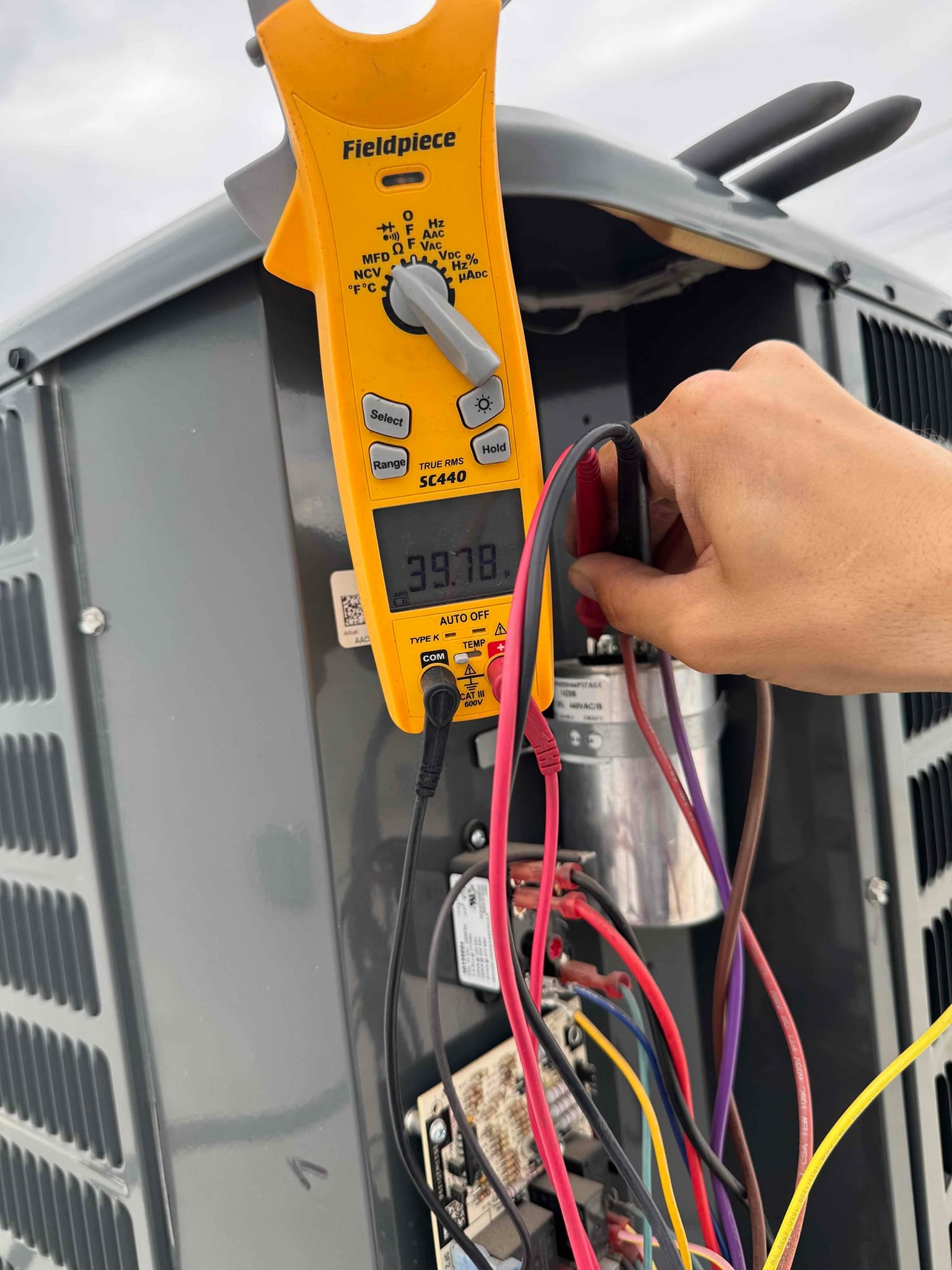 Clamp meter shows 39.78 V while test leads contact terminals on the dual-run capacitor inside the outdoor unit.