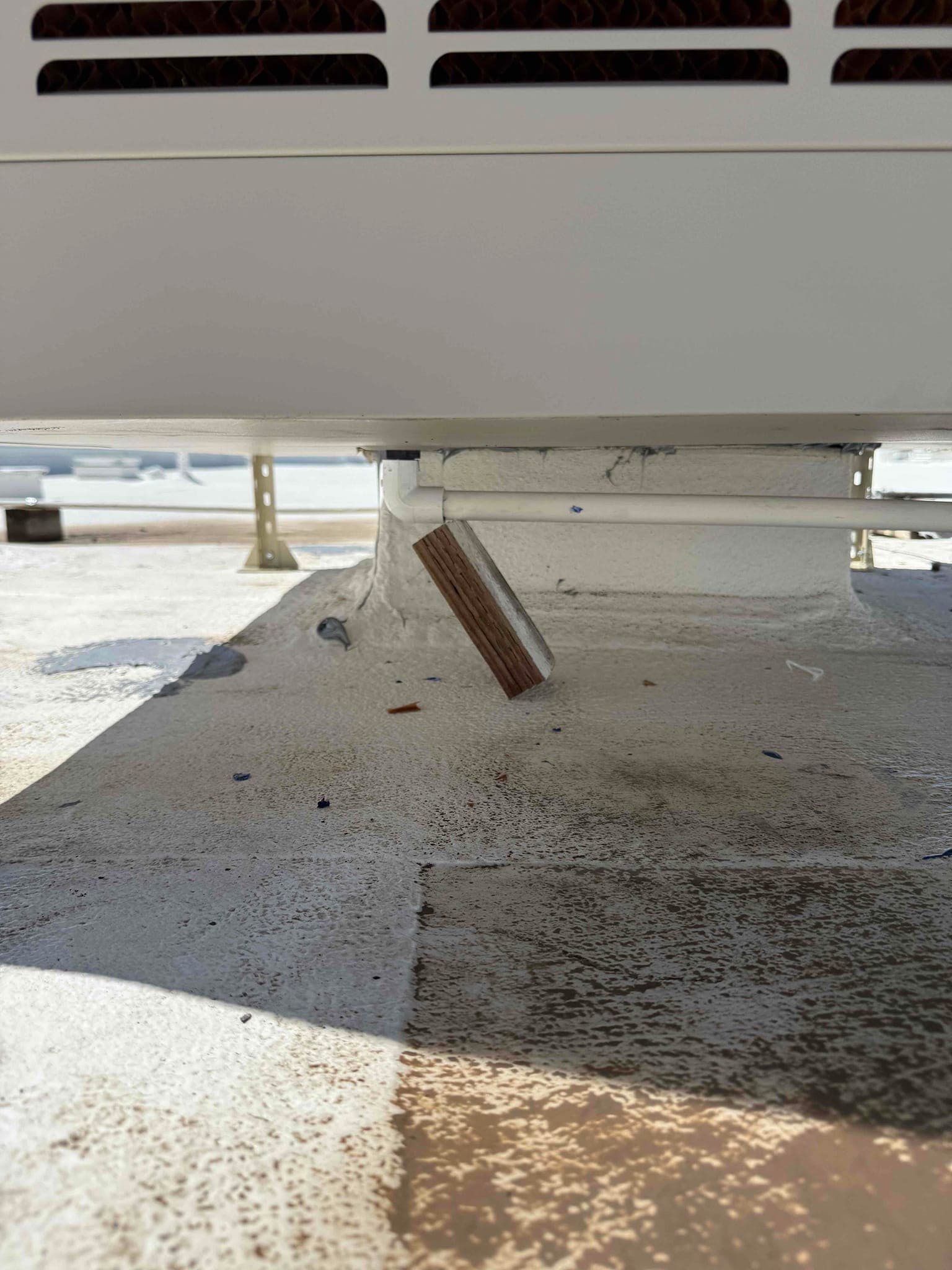 Condensate drain line exits below the newly set rooftop unit, discharging through a short angled outlet above the roof surface.