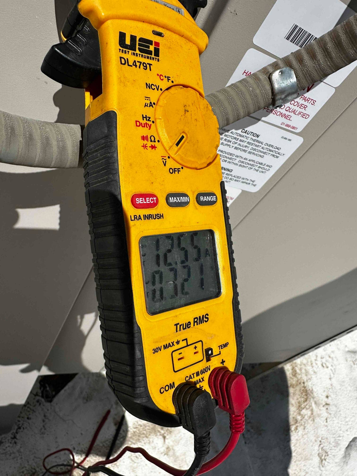 Digital multimeter connected at the outdoor unit shows a measurement on the display during electrical commissioning.