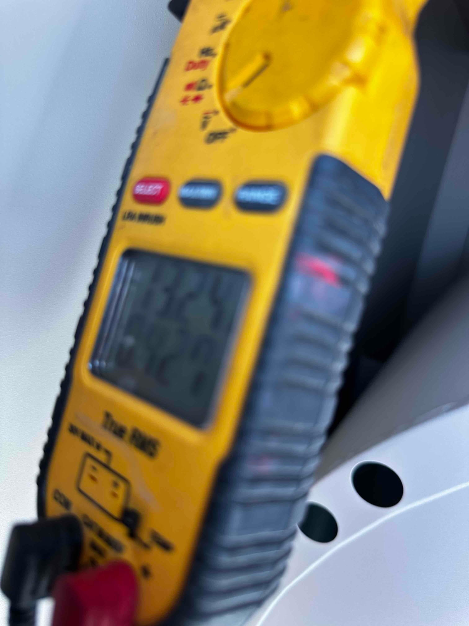 Digital multimeter connected with test leads during electrical checks on the HVAC installation.