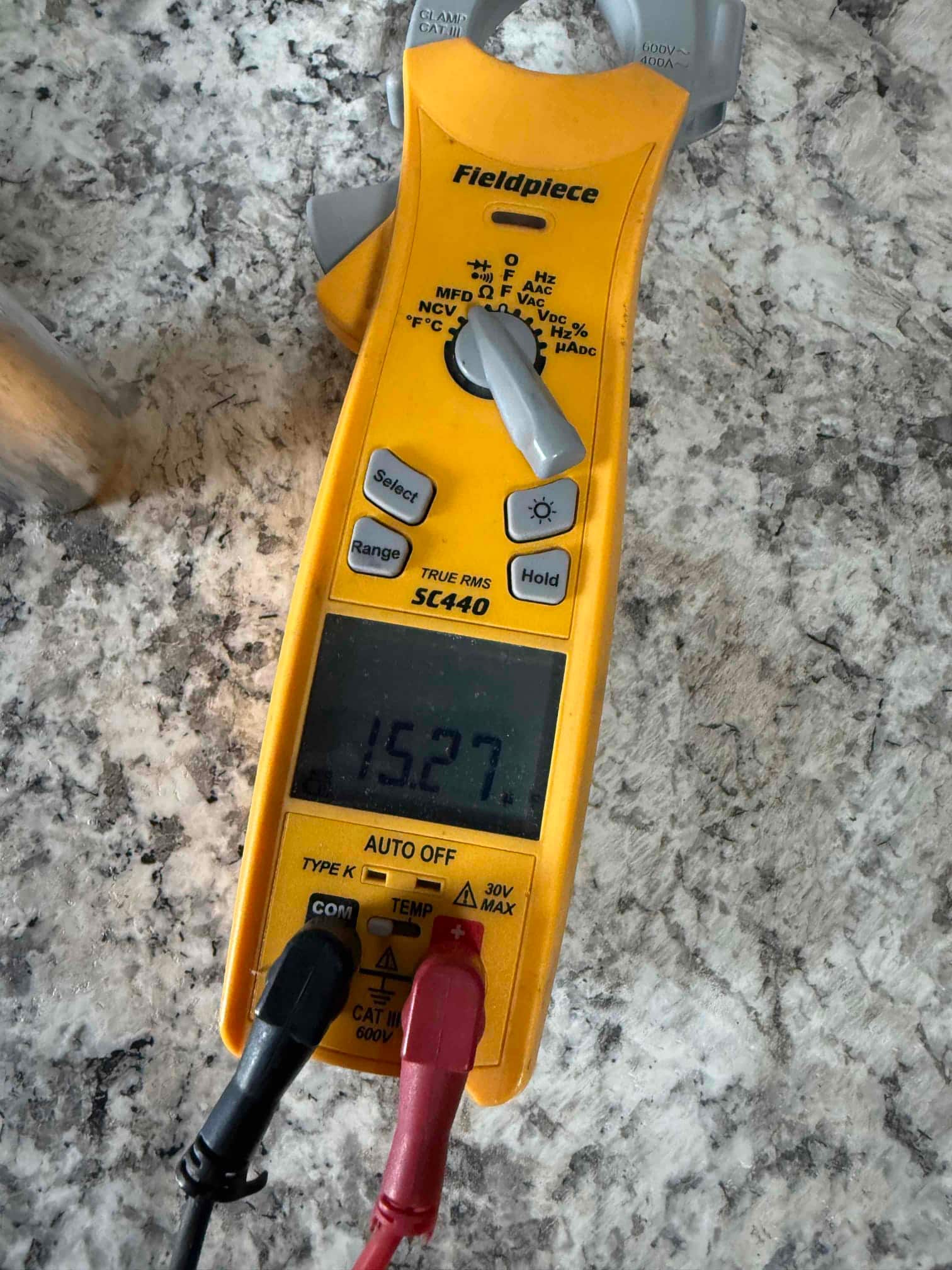 Digital multimeter displays 15.27 V with black and red probes connected to a circuit for measurement.