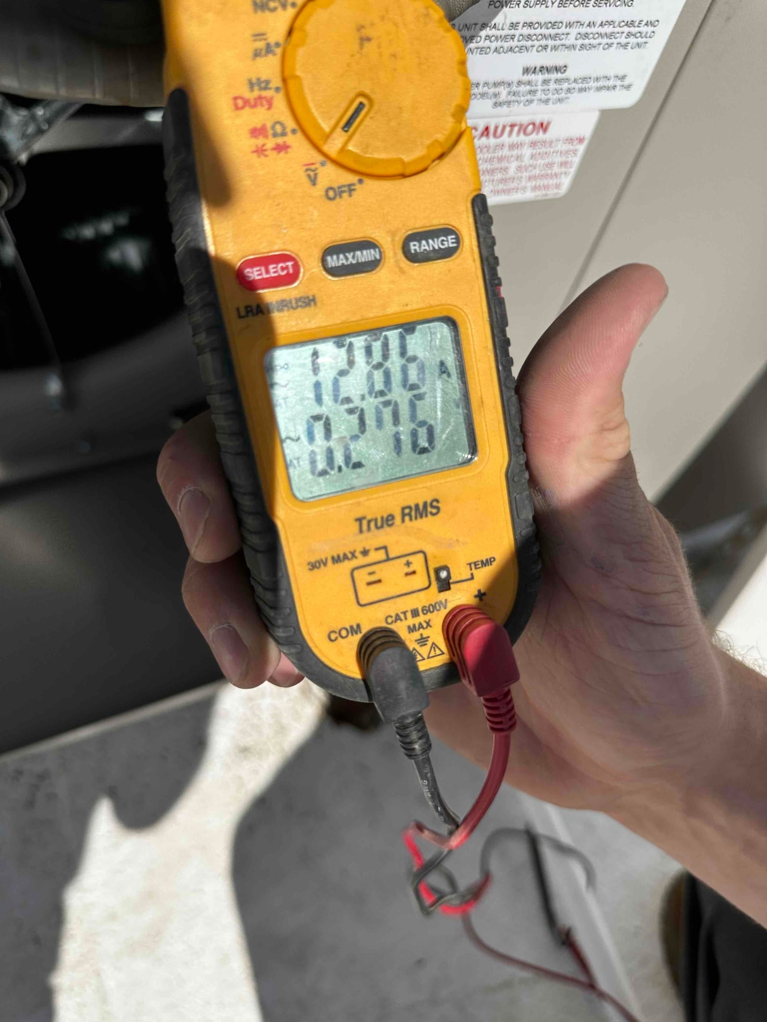 Digital multimeter displays 15.98 amps during electrical testing at the outdoor HVAC unit.