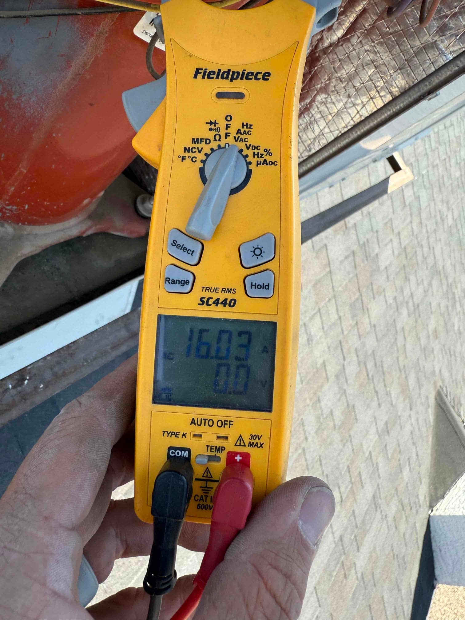 Digital multimeter displays 16.03 V with red and black probes connected to HVAC wiring at the outdoor unit.