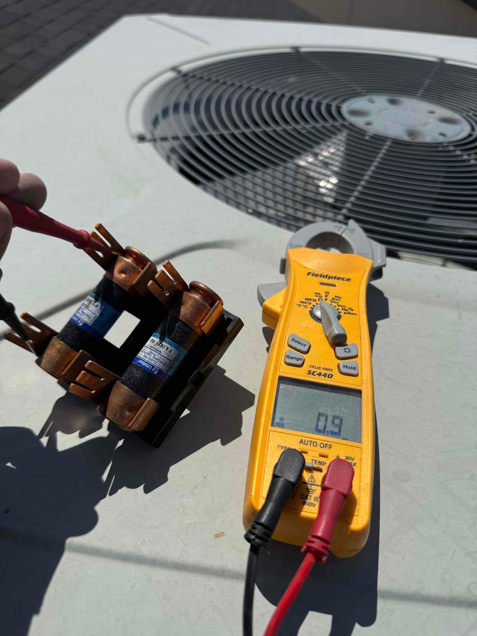 Digital multimeter measures 0.9 Ω across a fuse holder assembly on the outdoor condenser unit.