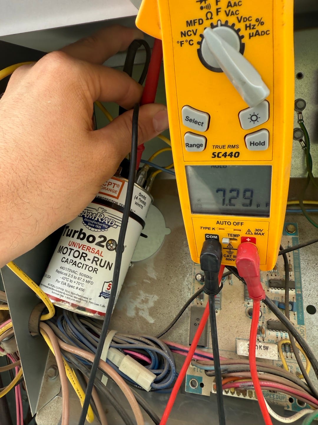 Digital multimeter measures 7.29 V across the motor-run capacitor terminals inside the outdoor condenser control compartment.