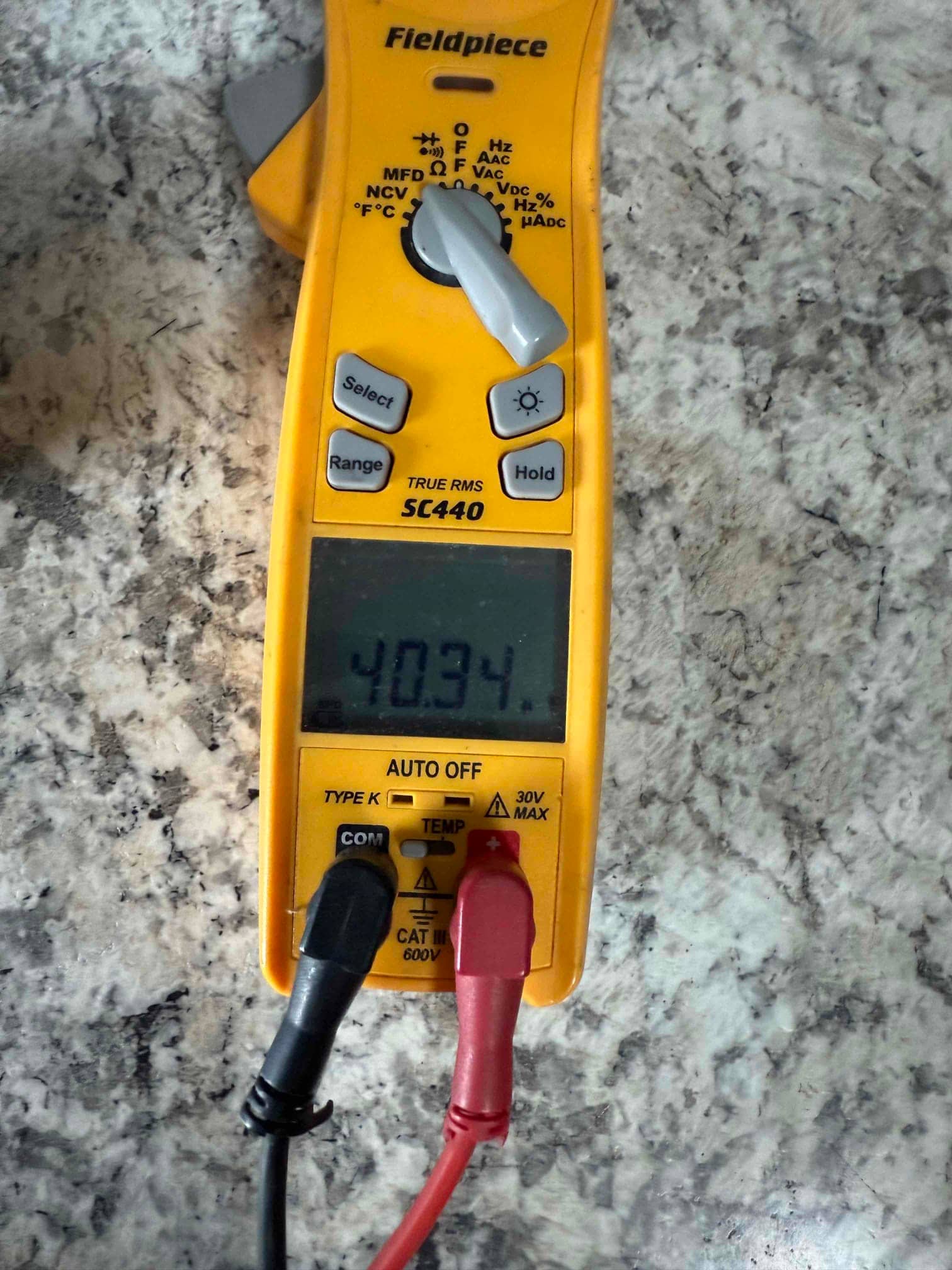 Digital multimeter measures a capacitor at 40.34 µF using red and black test leads on a work surface.