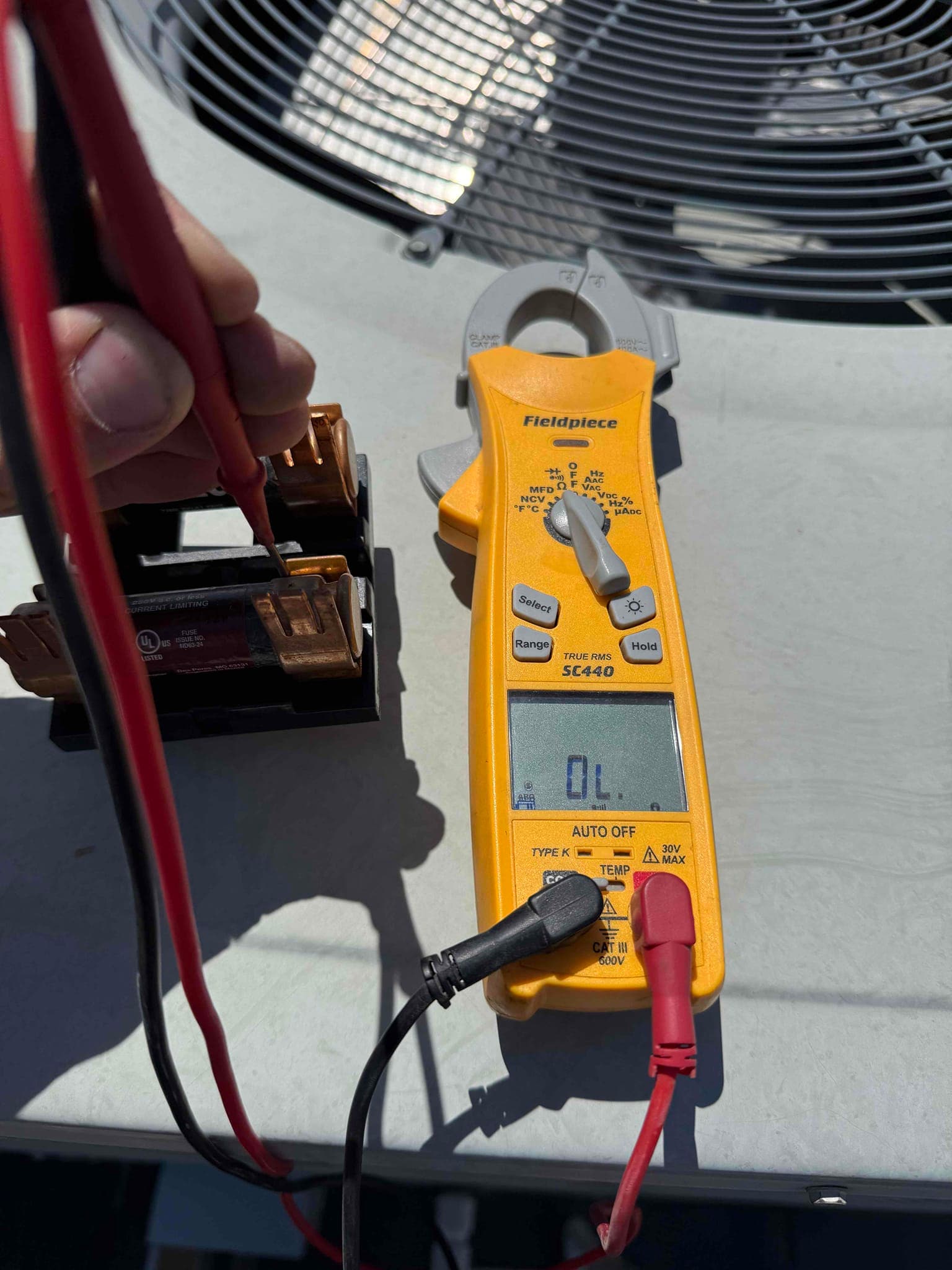 Digital multimeter set to resistance shows OL while testing a cartridge fuse with red and black probes.