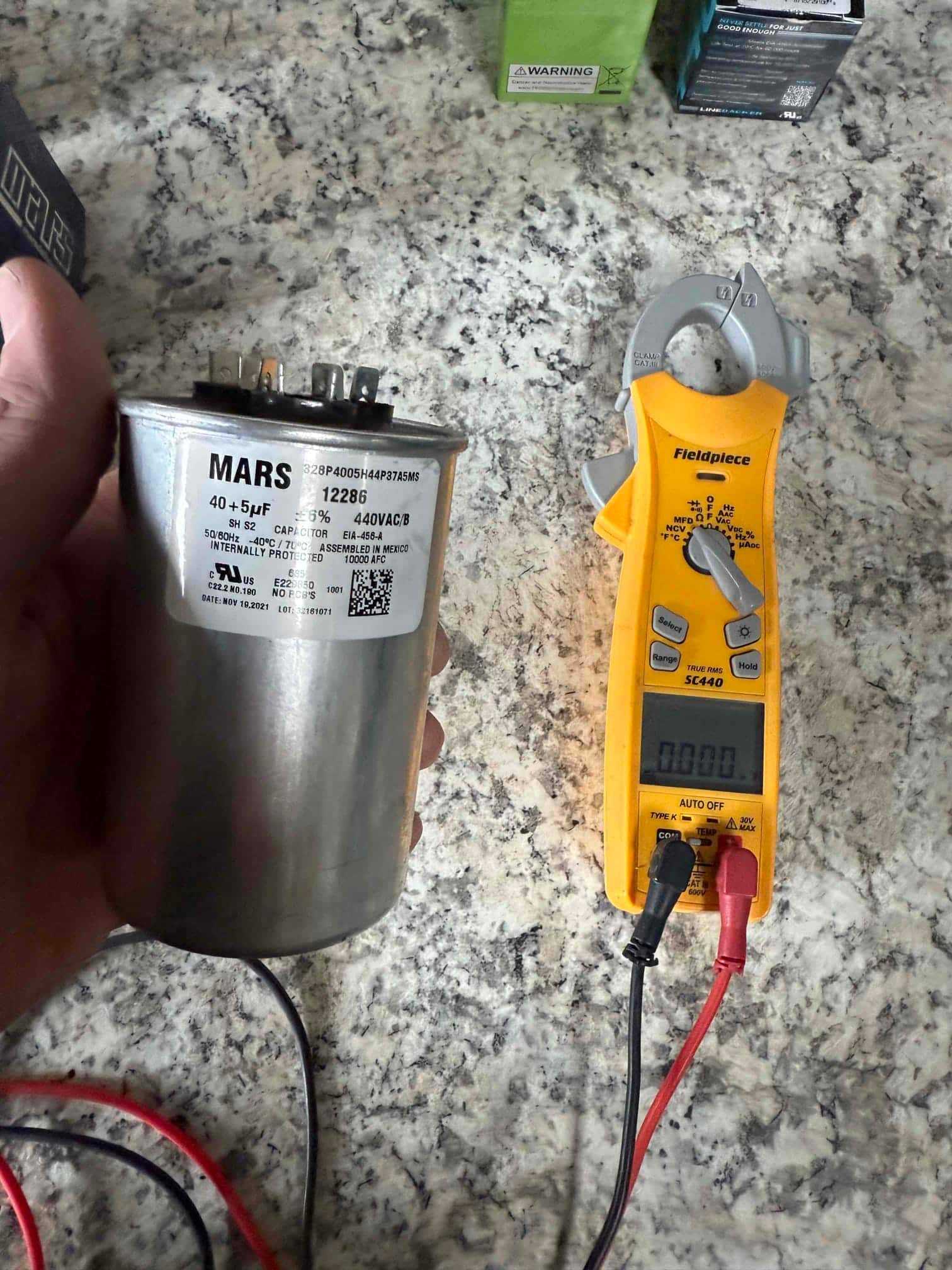 Digital multimeter shows 0.00 V with test leads connected next to a 40 + 5 μF dual-run capacitor.