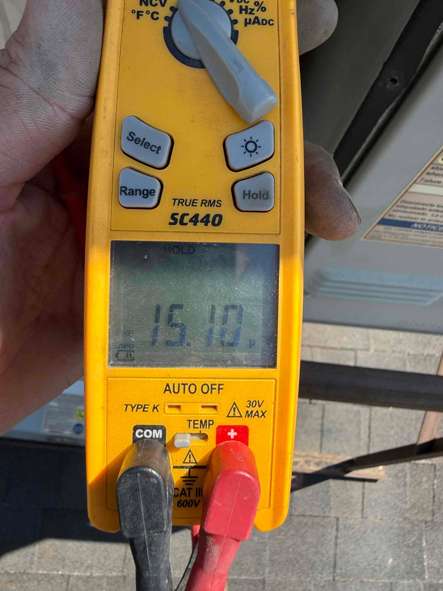 Digital multimeter shows 15.10 V on the display with black and red probes connected to the test leads.