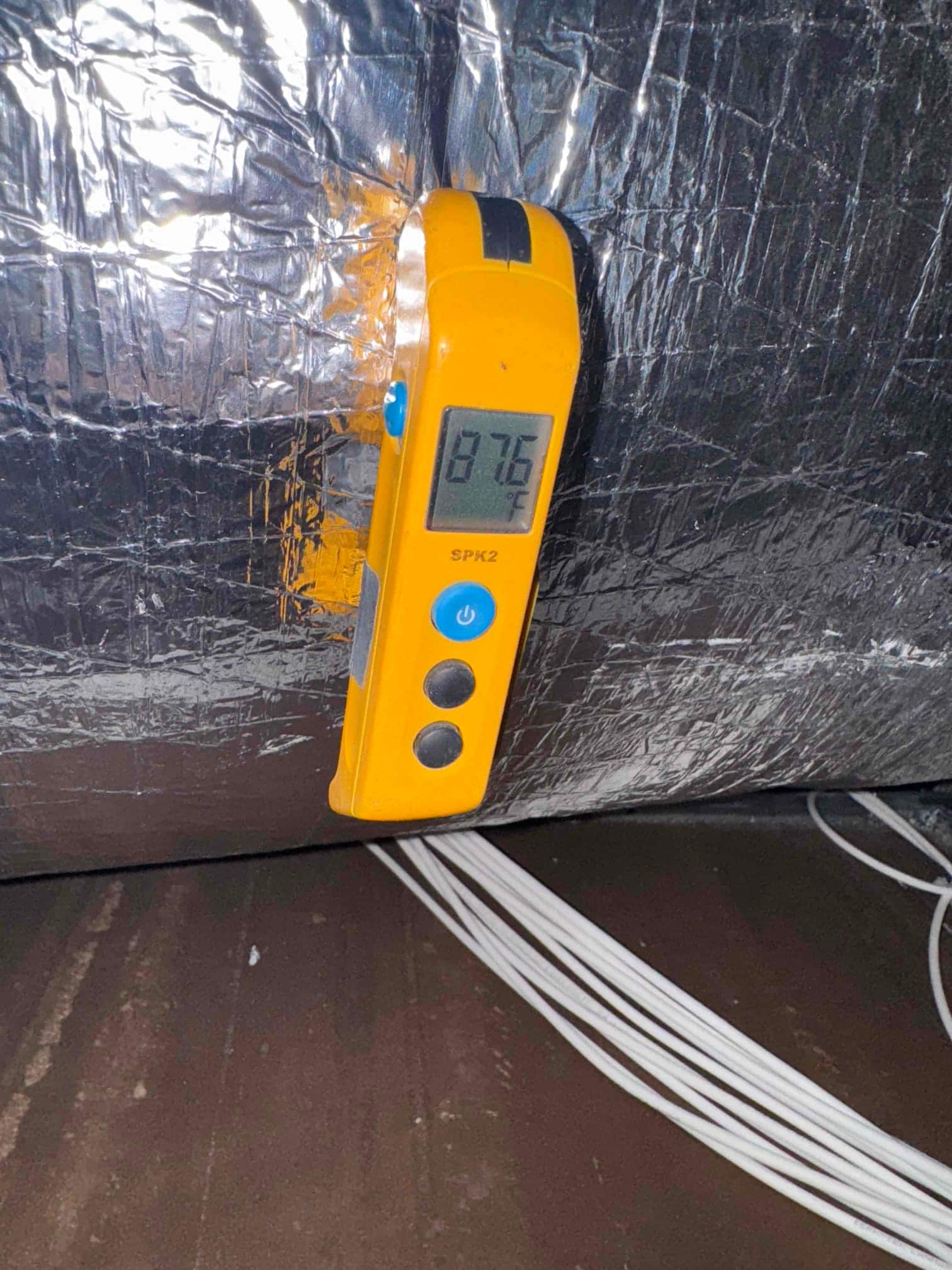 Digital thermometer attached to insulated duct shows 87.6 °F on the display, indicating duct surface temperature during operation.