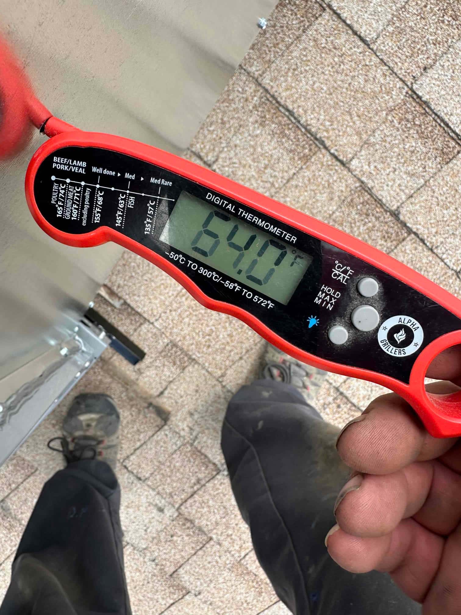 Digital thermometer displays 64°F while checking air temperature during commissioning near the rooftop package unit.