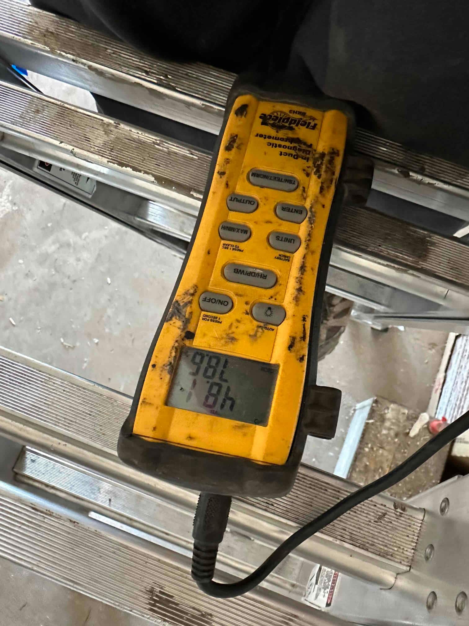 Digital thermometer on a ladder shows air temperature during commissioning of the mini‑split system.