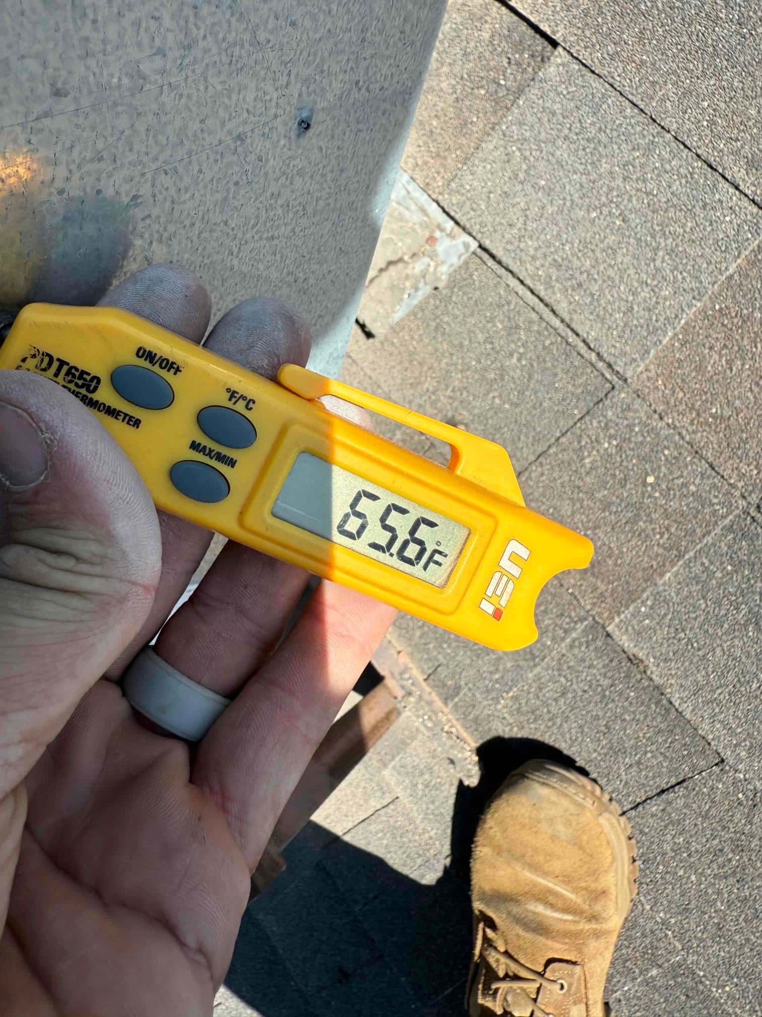 Digital thermometer shows 65.6 °F while measuring the surface temperature of HVAC equipment during diagnostic evaluation.