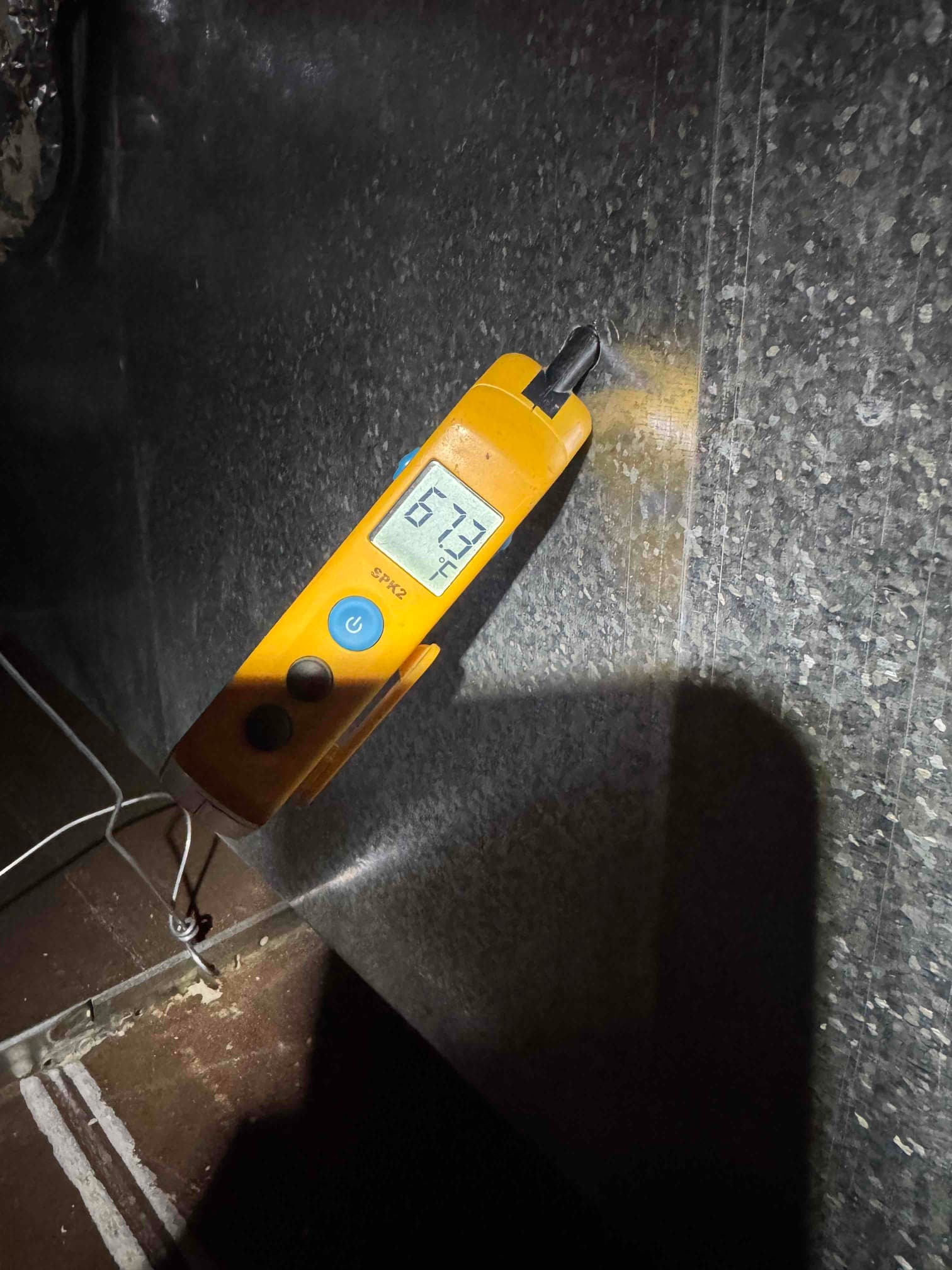 Digital thermometer shows 67.3 °F while measuring air temperature at the surface of a metal duct.