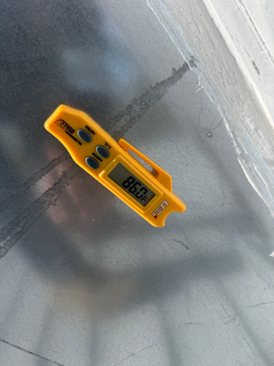 Digital thermometer shows 86.0 °F surface temperature on a sheet-metal HVAC component during the repair.